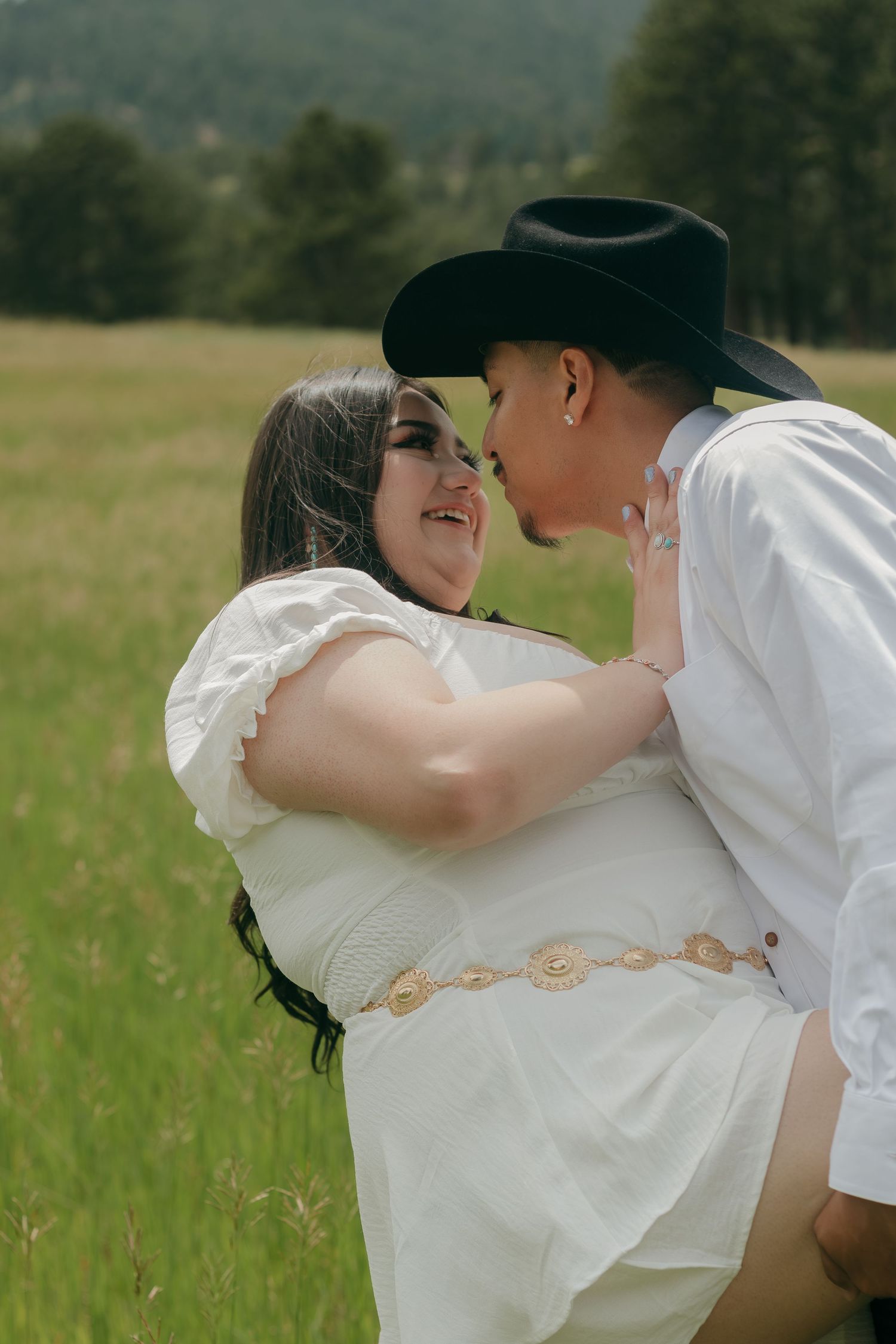 Sweet embrace between couple in western-themed outfits standing in mountain meadow.