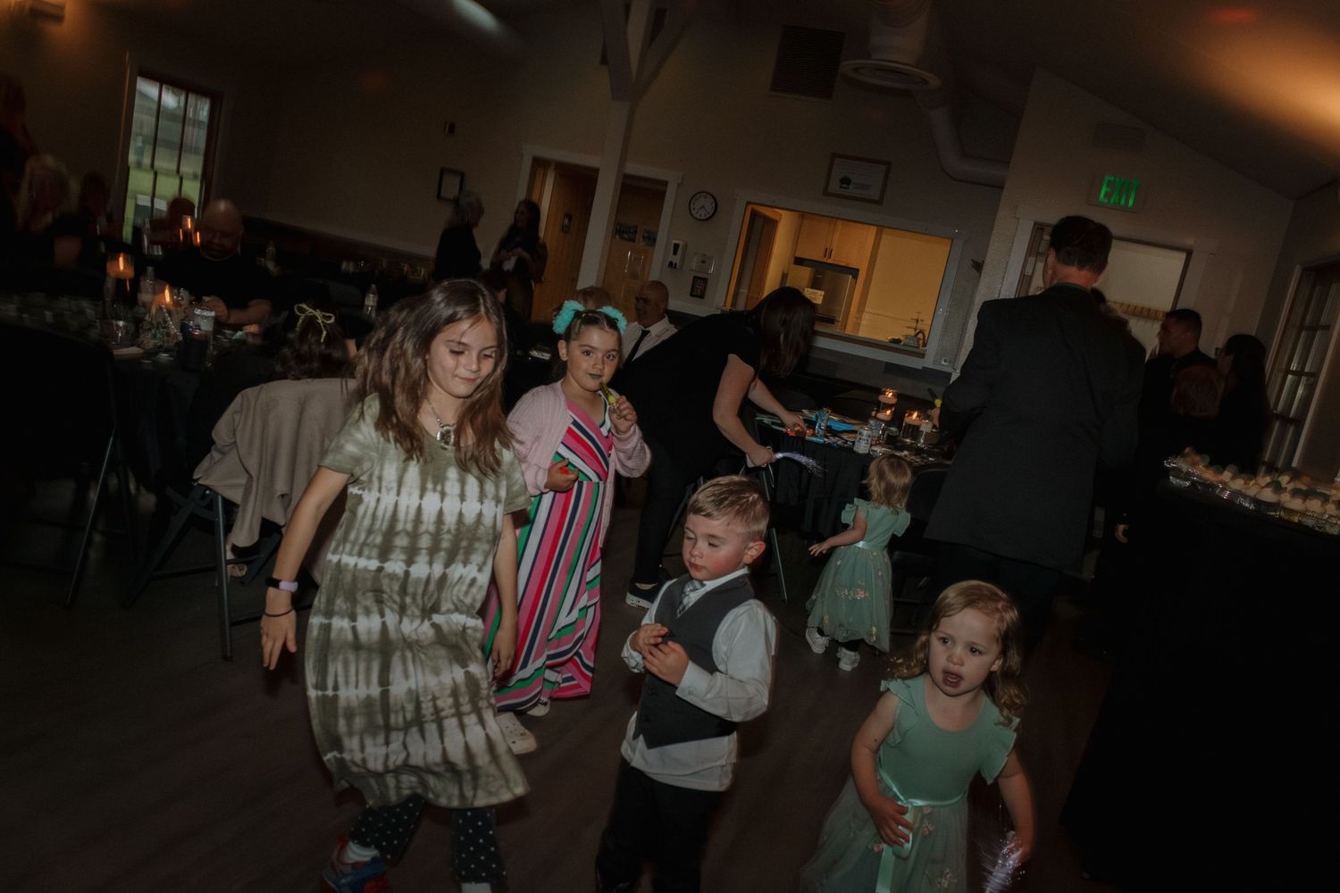 Guests dancing and socializing at a lively indoor wedding reception with dim lighting.