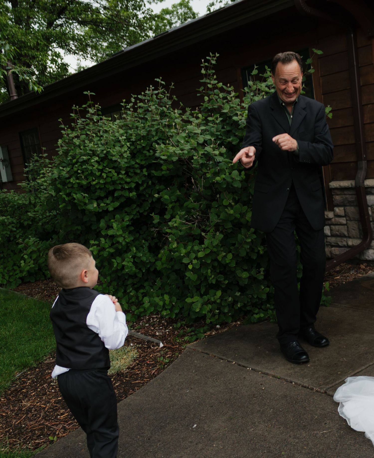 A young ring bearer in formal attire interacts with a guest on a garden path.