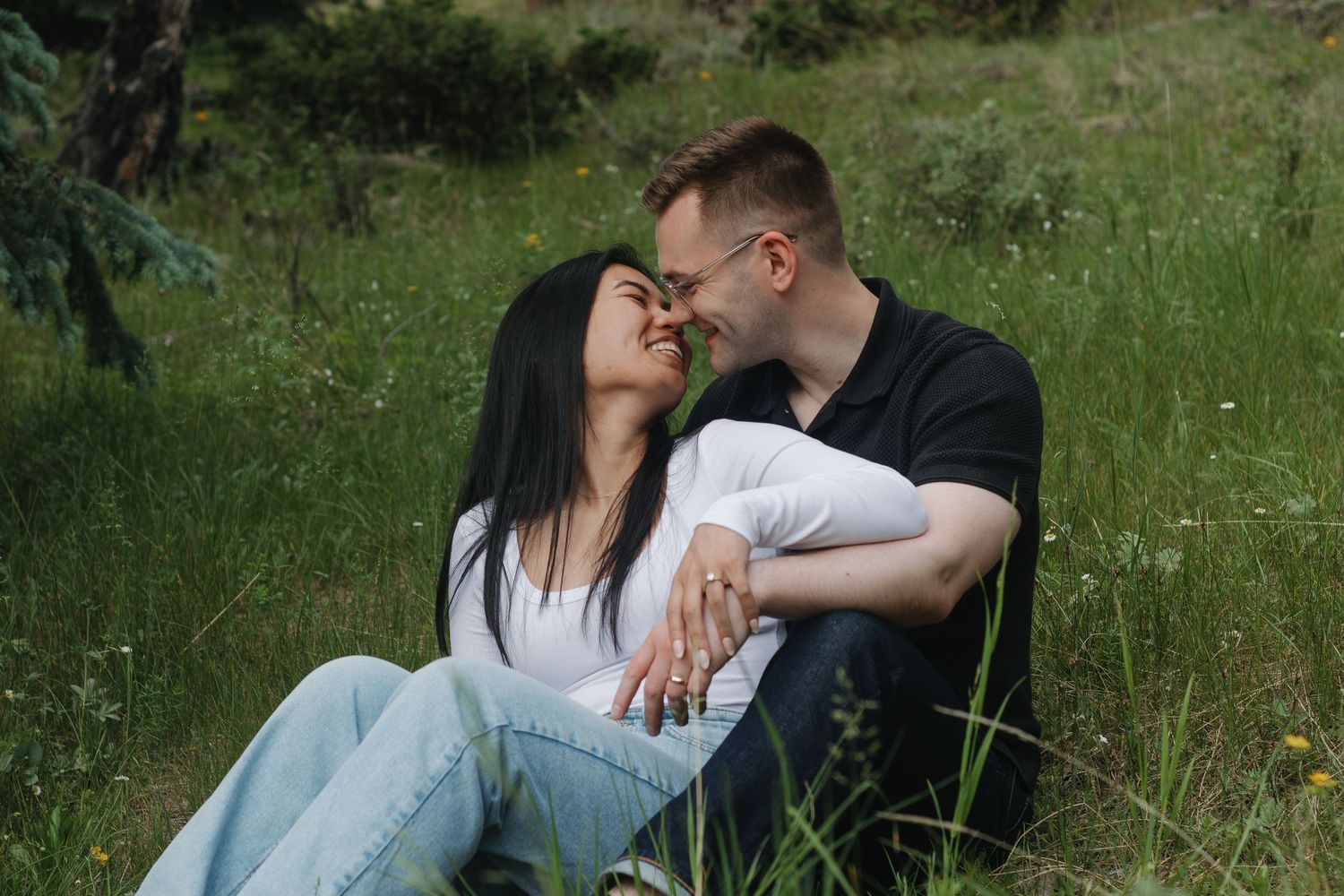 A romantic couple embraces while relaxing in tall grass on a mountainside.