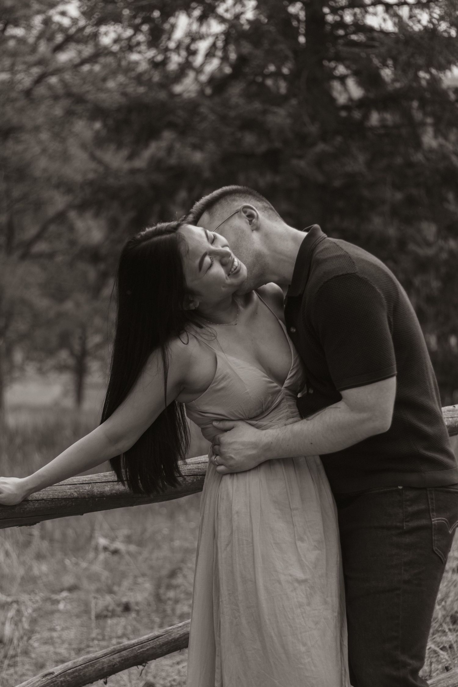 A romantic couple embraces against a wooden fence in a dreamy black and white outdoor photoshoot.