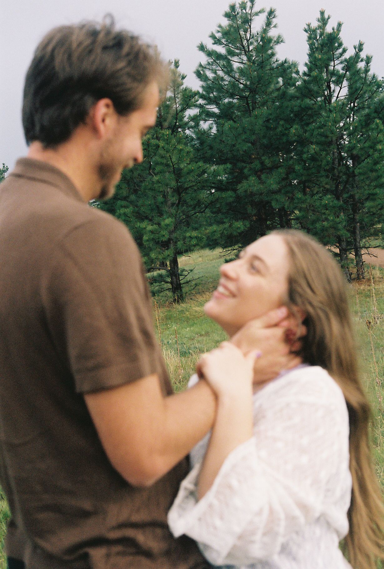 Happy woman smiling up at her partner while he gently touches her face in a pine forest meadow.