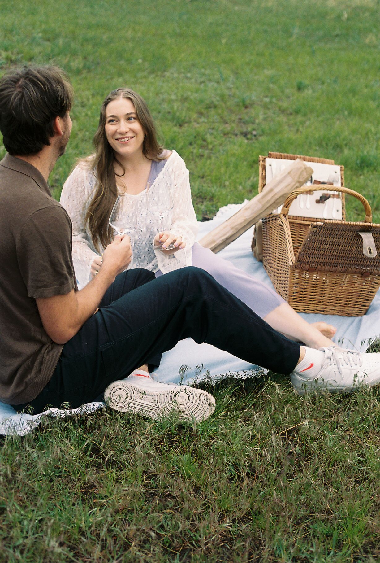 Couple enjoying a romantic picnic on a blanket in a green park with a wicker basket nearby.