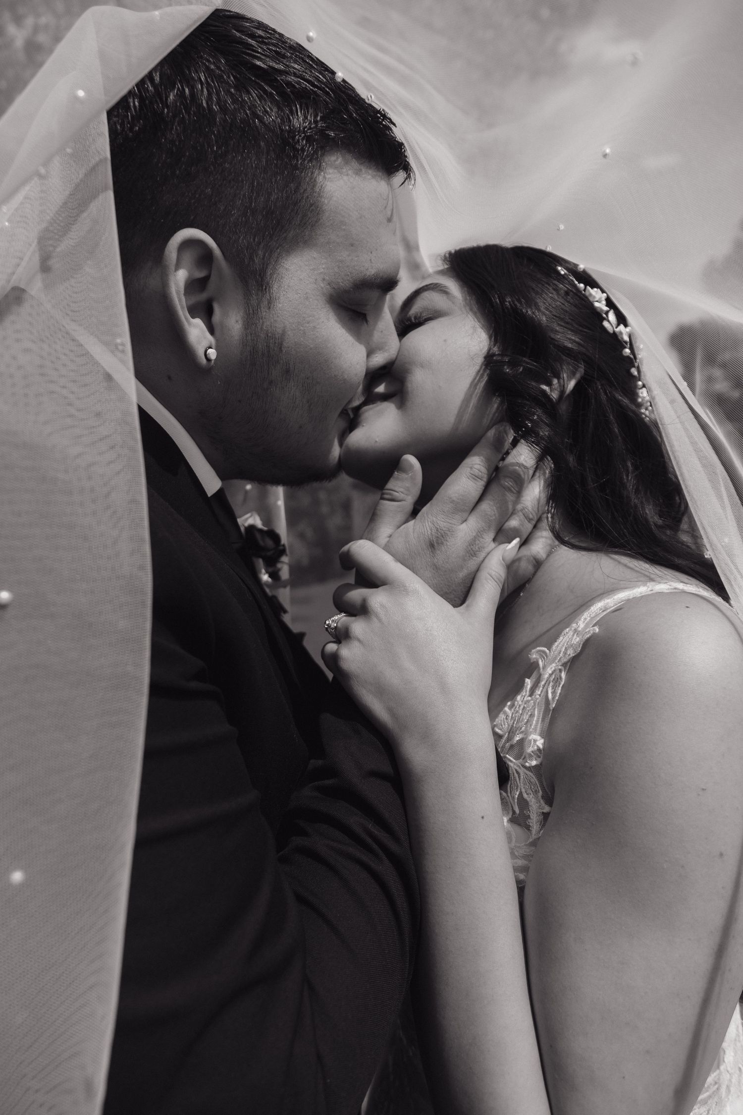 Black and white close-up of bride and groom sharing a romantic kiss under veil.