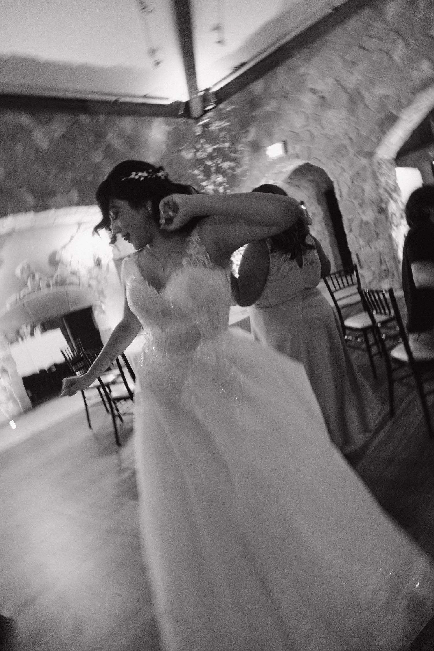 Bride sharing an emotional hug with bridesmaid on the dance floor in black and white.