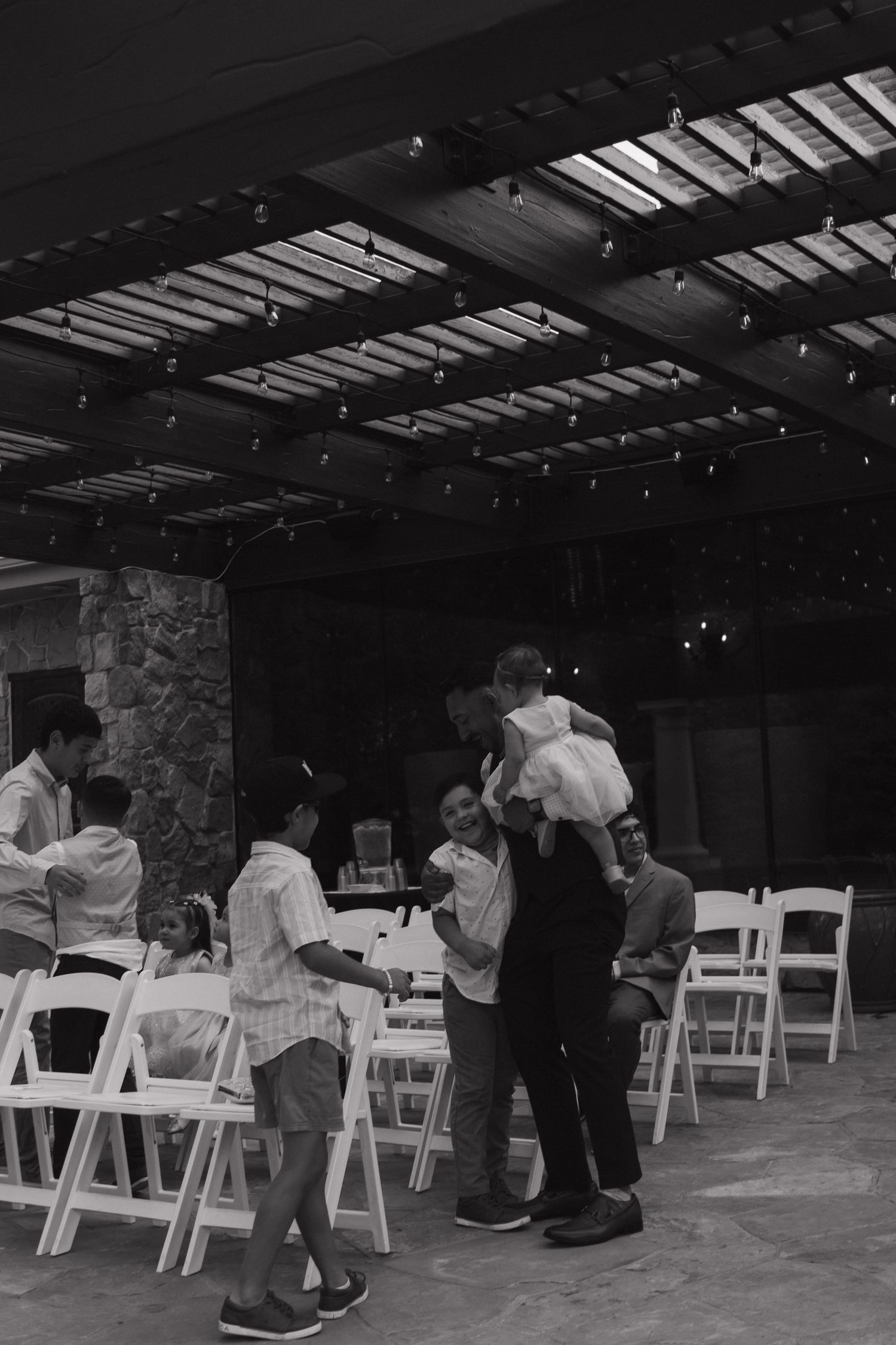 Guests mingle under string lights at an elegant outdoor wedding venue with white folding chairs.