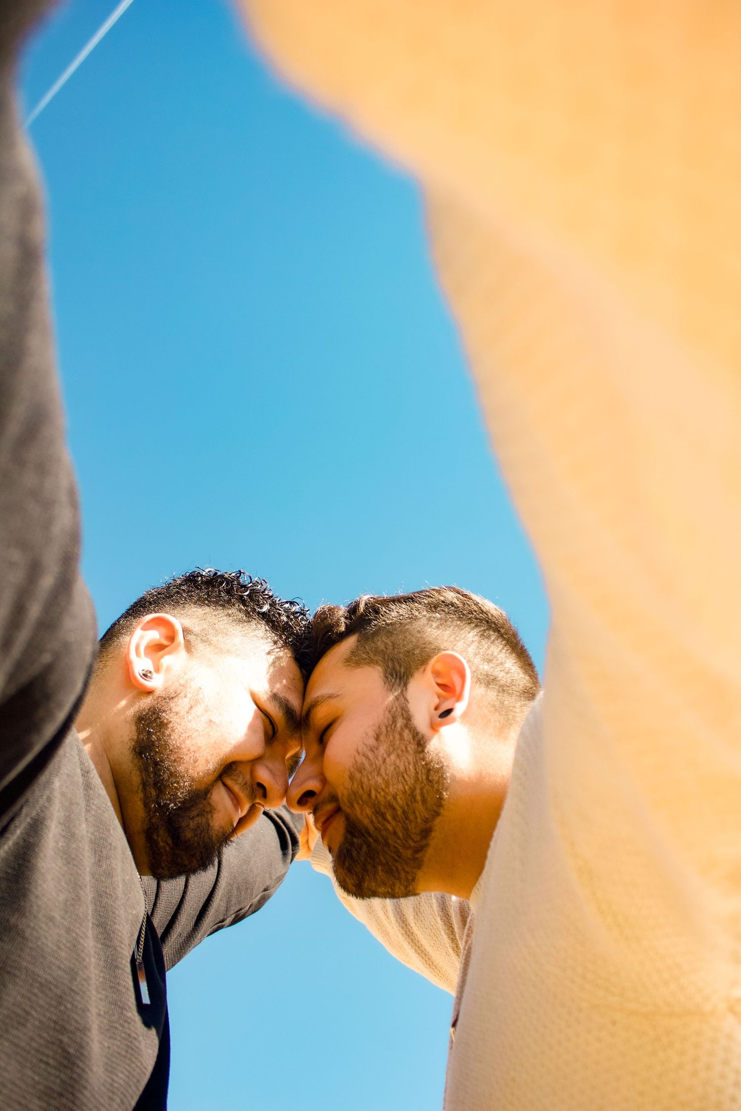 Intimate close-up of two people touching foreheads against vibrant sky.