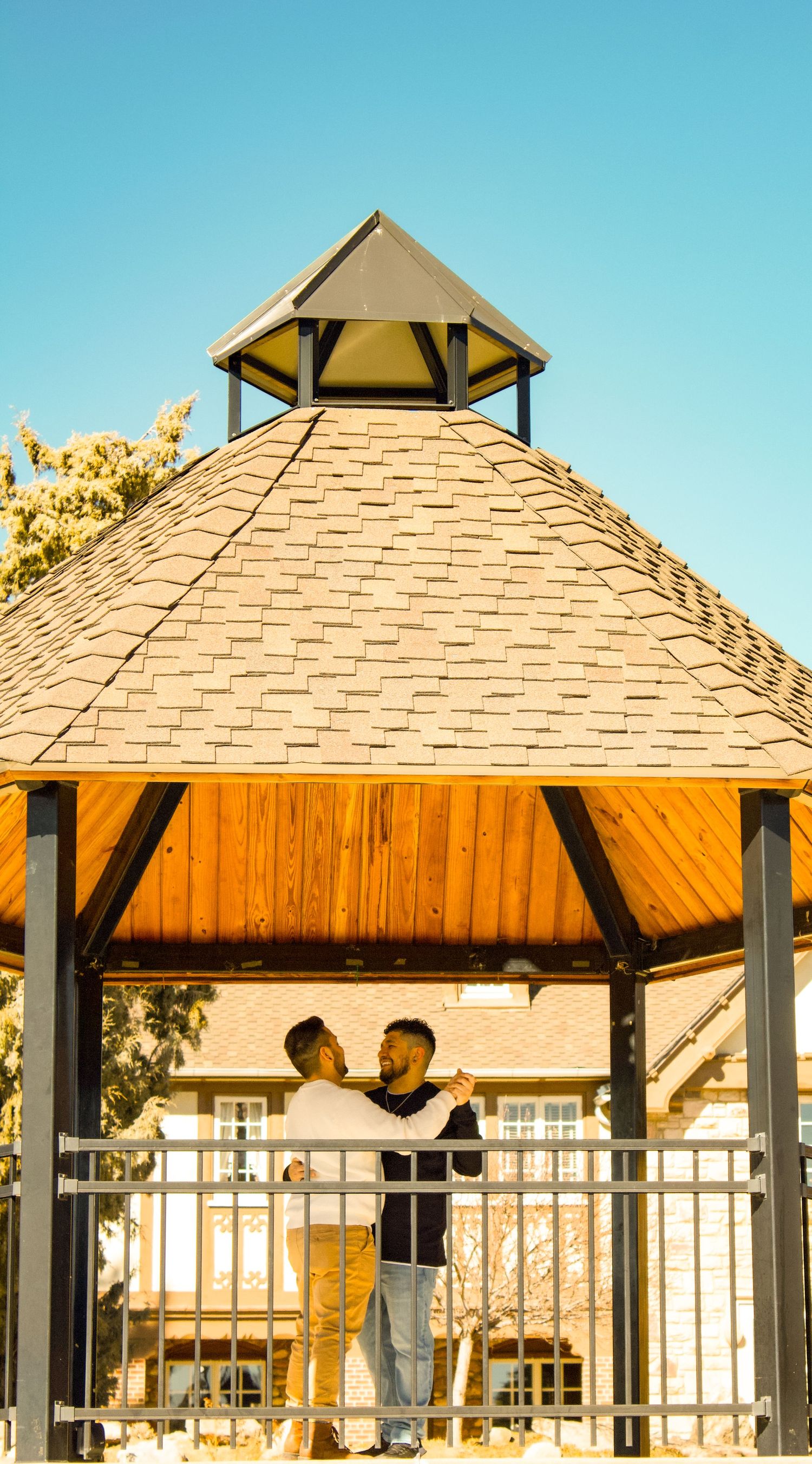 Wooden gazebo with shingled roof and pillars against bright blue sky at luxury estate.