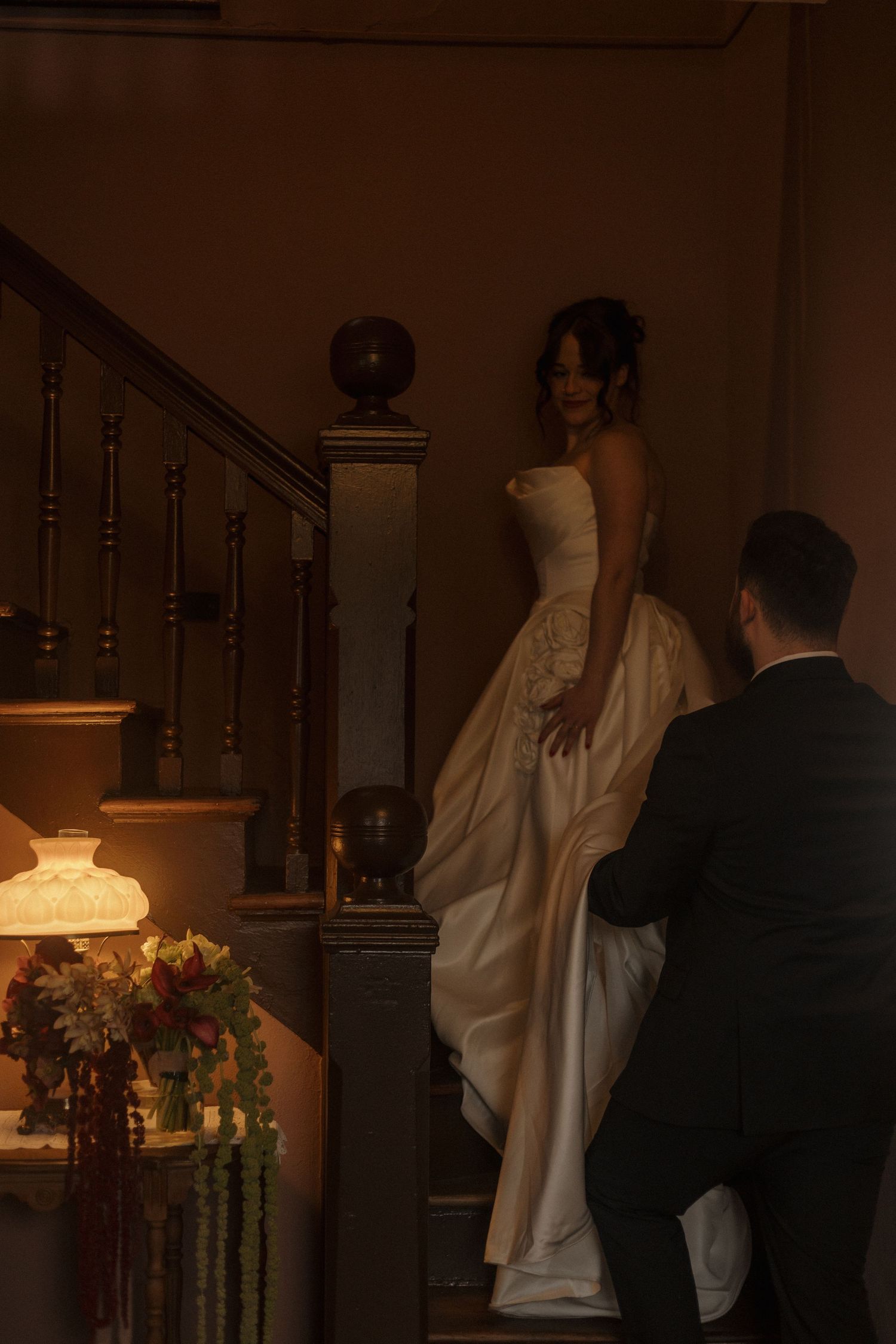 A romantic indoor wedding ceremony with dramatic lighting and floral arrangements near a staircase.