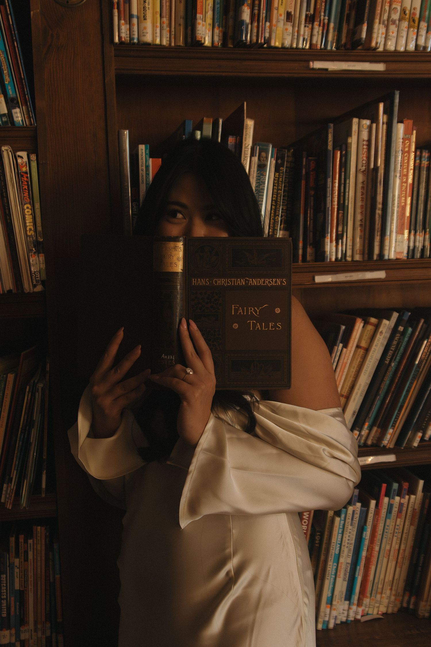 Person in white clothing browsing books on wooden library shelves.