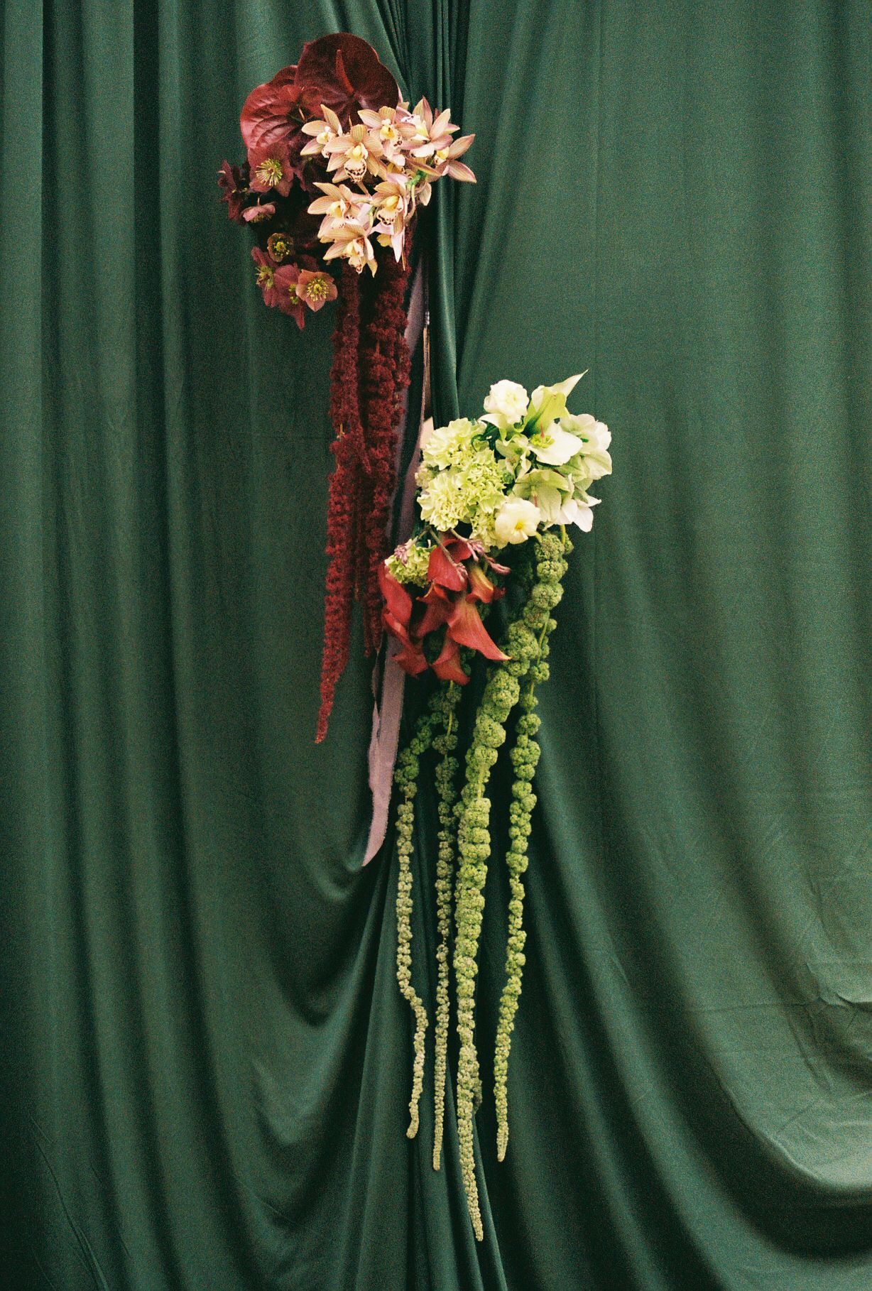Elegant floral arrangement with hanging amaranthus and mixed flowers against a green backdrop.