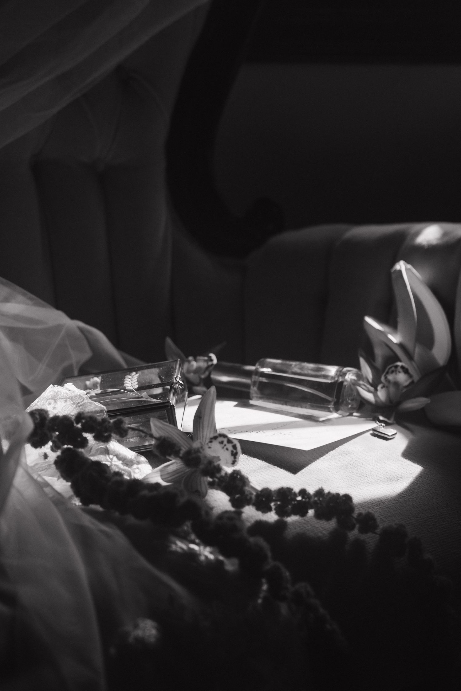 Black and white still life of jewelry and accessories arranged on a light surface with delicate fabric.