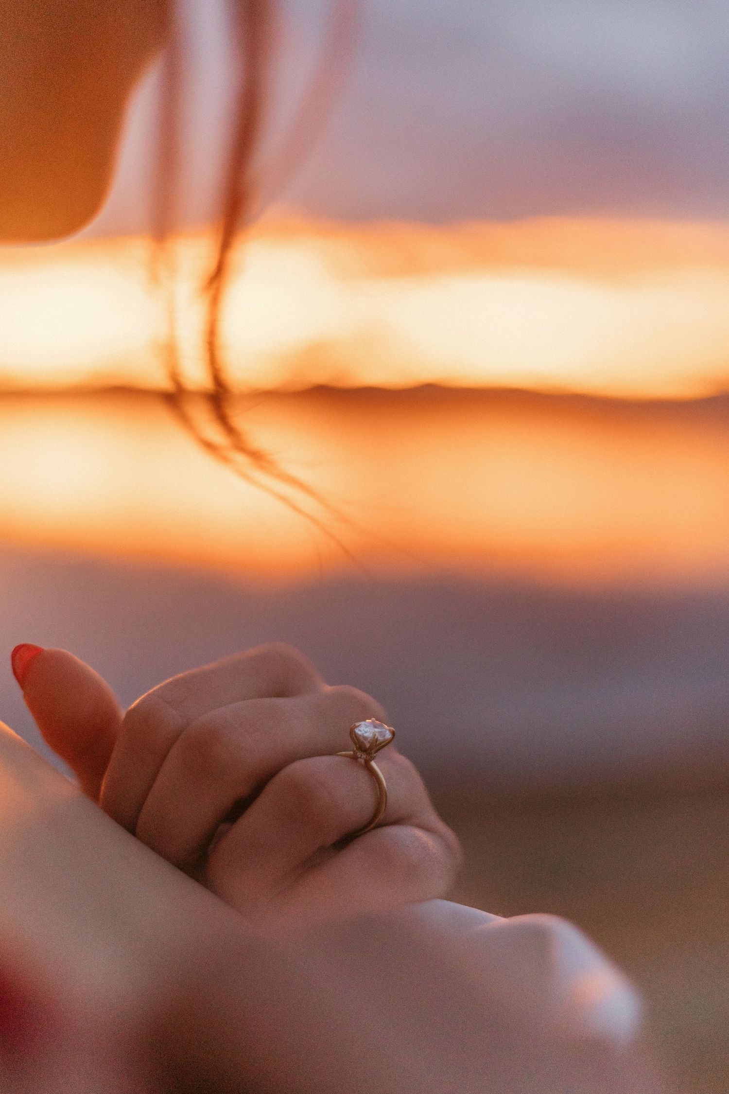 An engagement ring sparkles on a hand silhouetted against a golden sunset.