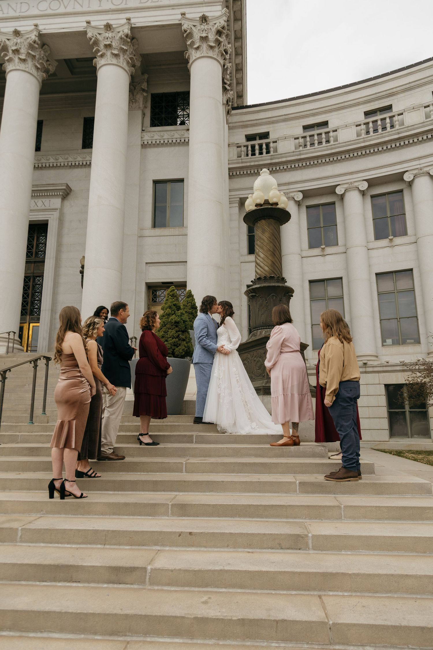 Wedding party members stand on the steps of a historic building with classical architecture.