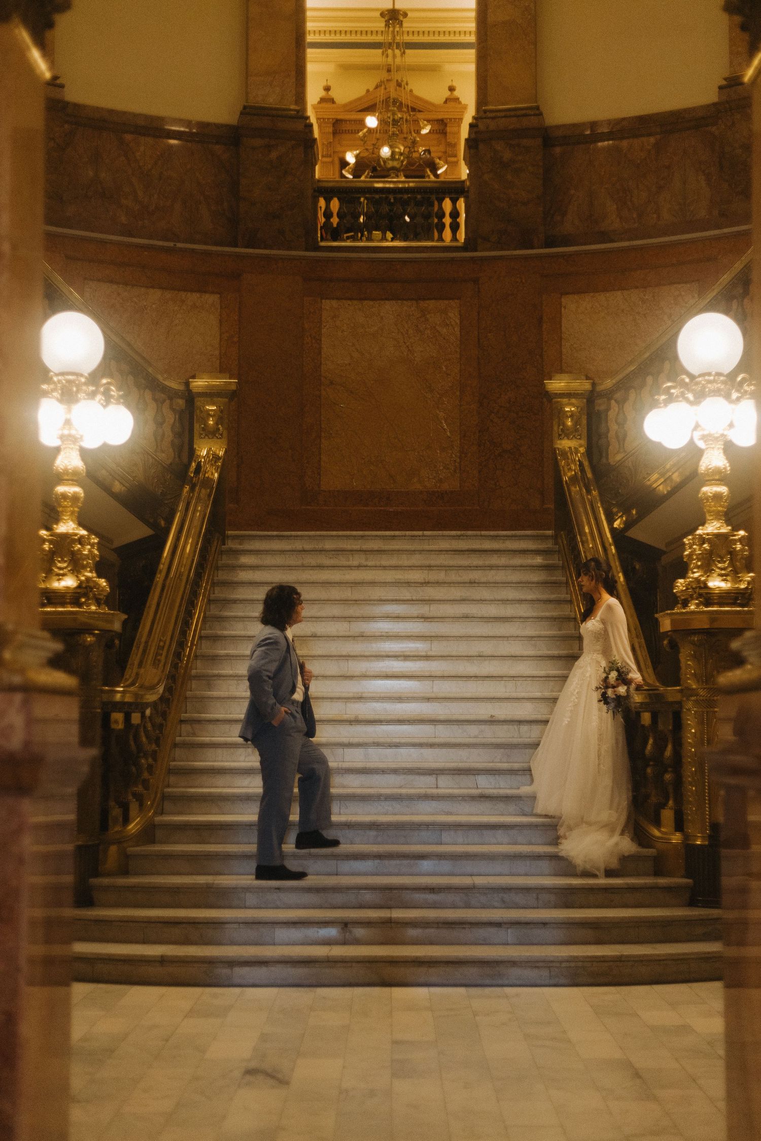 An intimate wedding ceremony unfolds on an elegant marble staircase lit by vintage wall sconces.