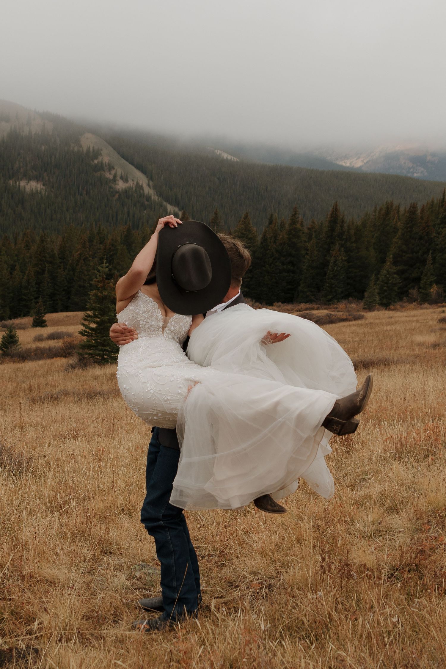 Couple performs romantic dip pose in a mountain meadow during their wedding.