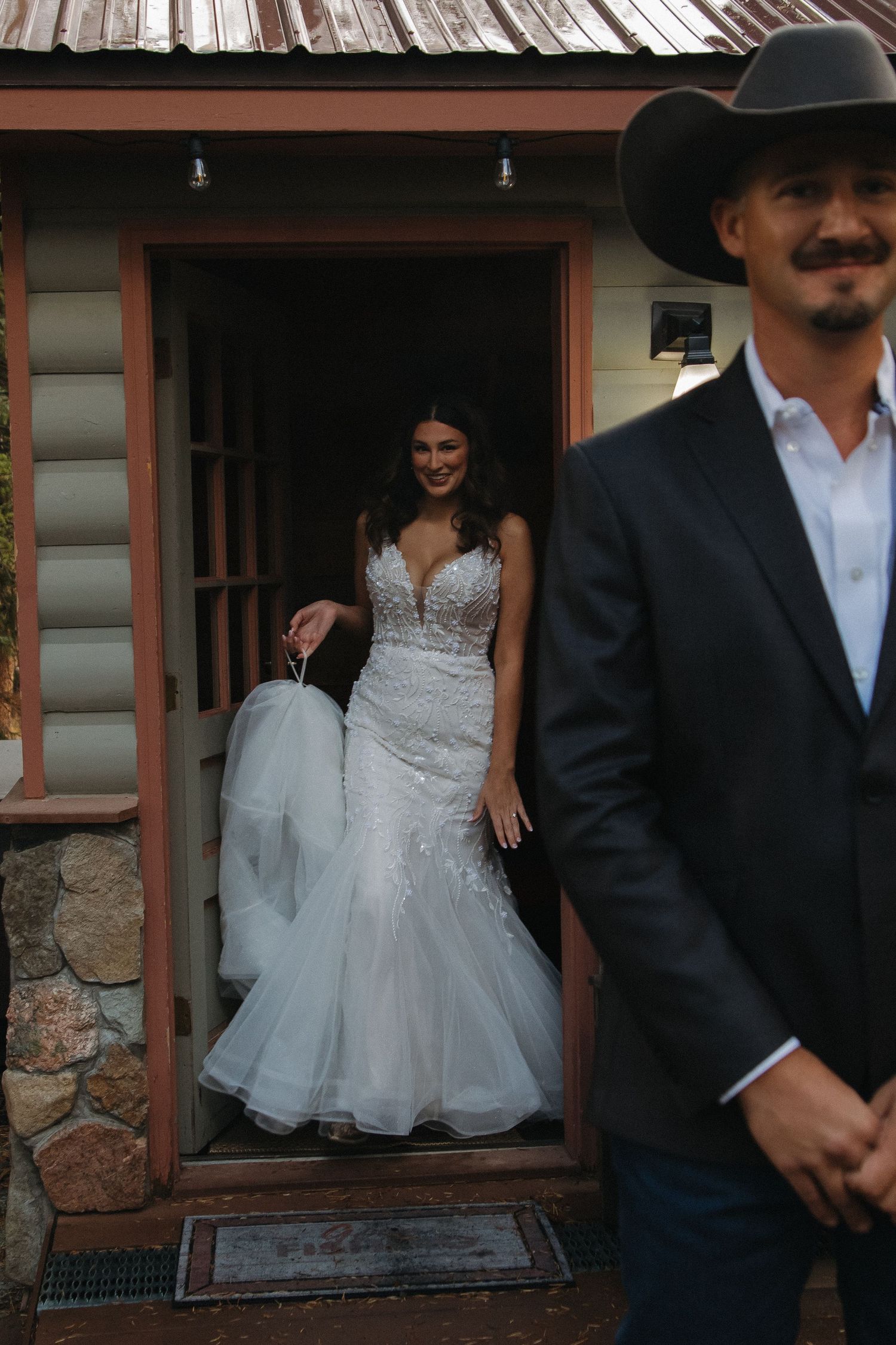 A white wedding dress is visible through a rustic cabin window frame.