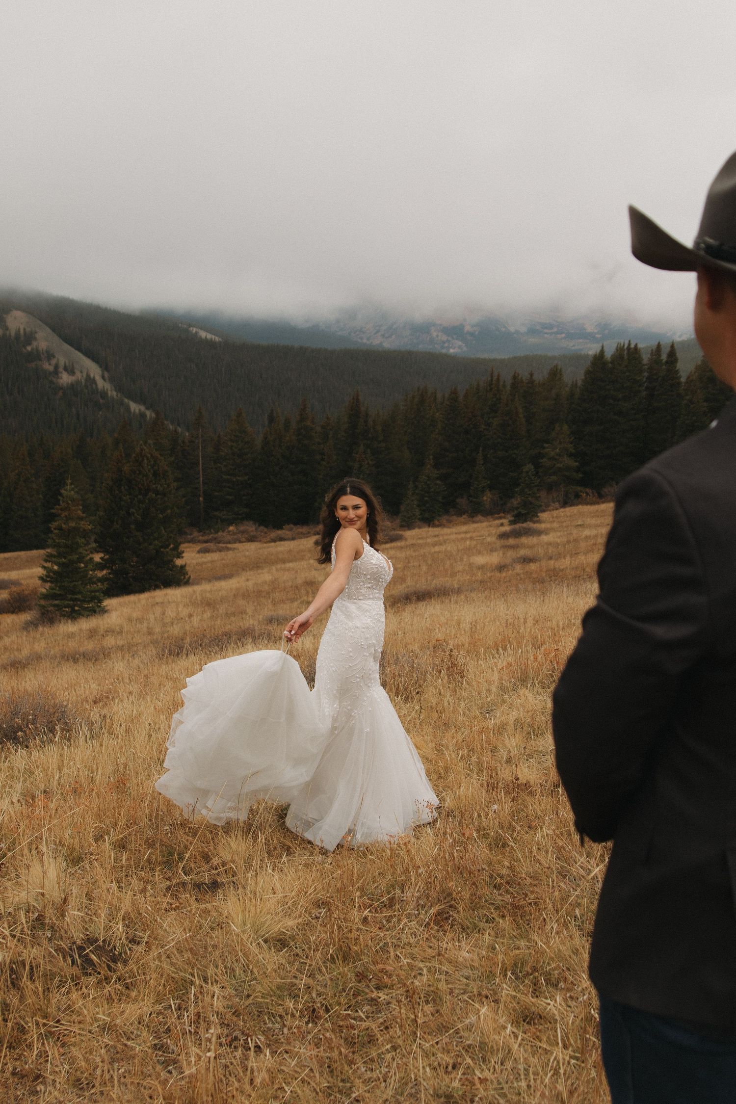 A flowing white wedding dress twirls against a mountainous autumn landscape.