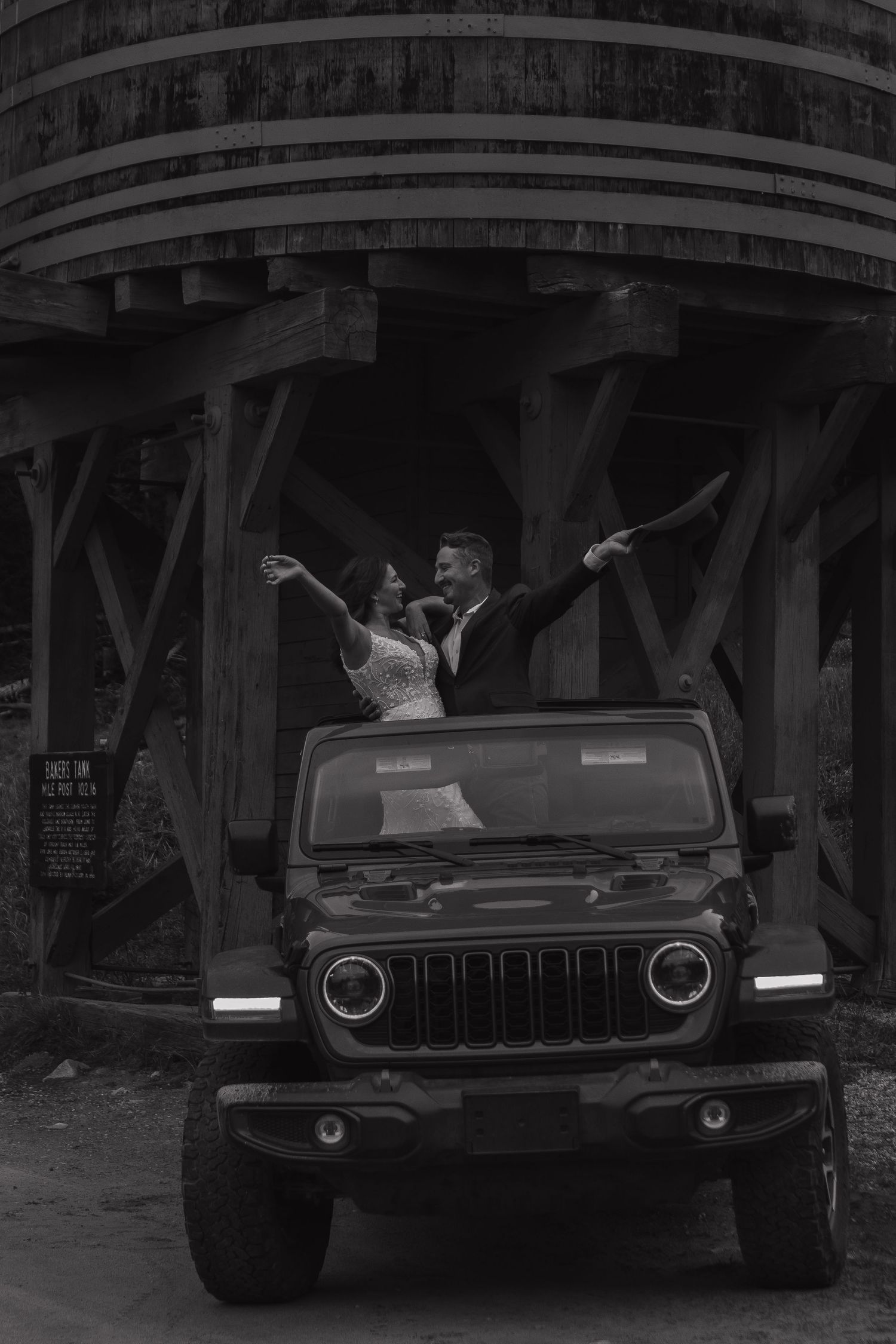 Black vintage car parked under a wooden bridge structure creates dramatic silhouette.