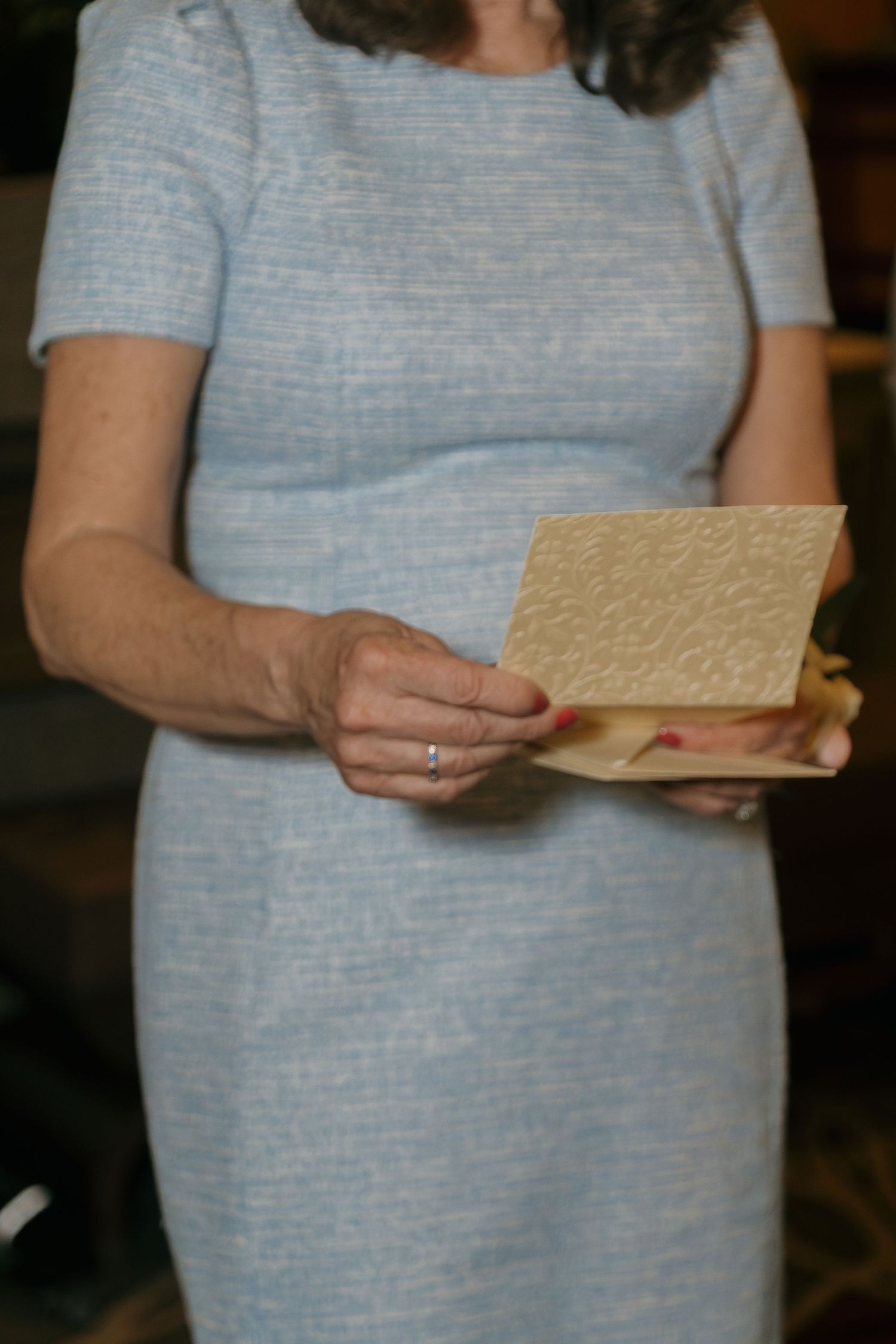 Woman in light blue dress holds decorative envelope at formal wedding event.