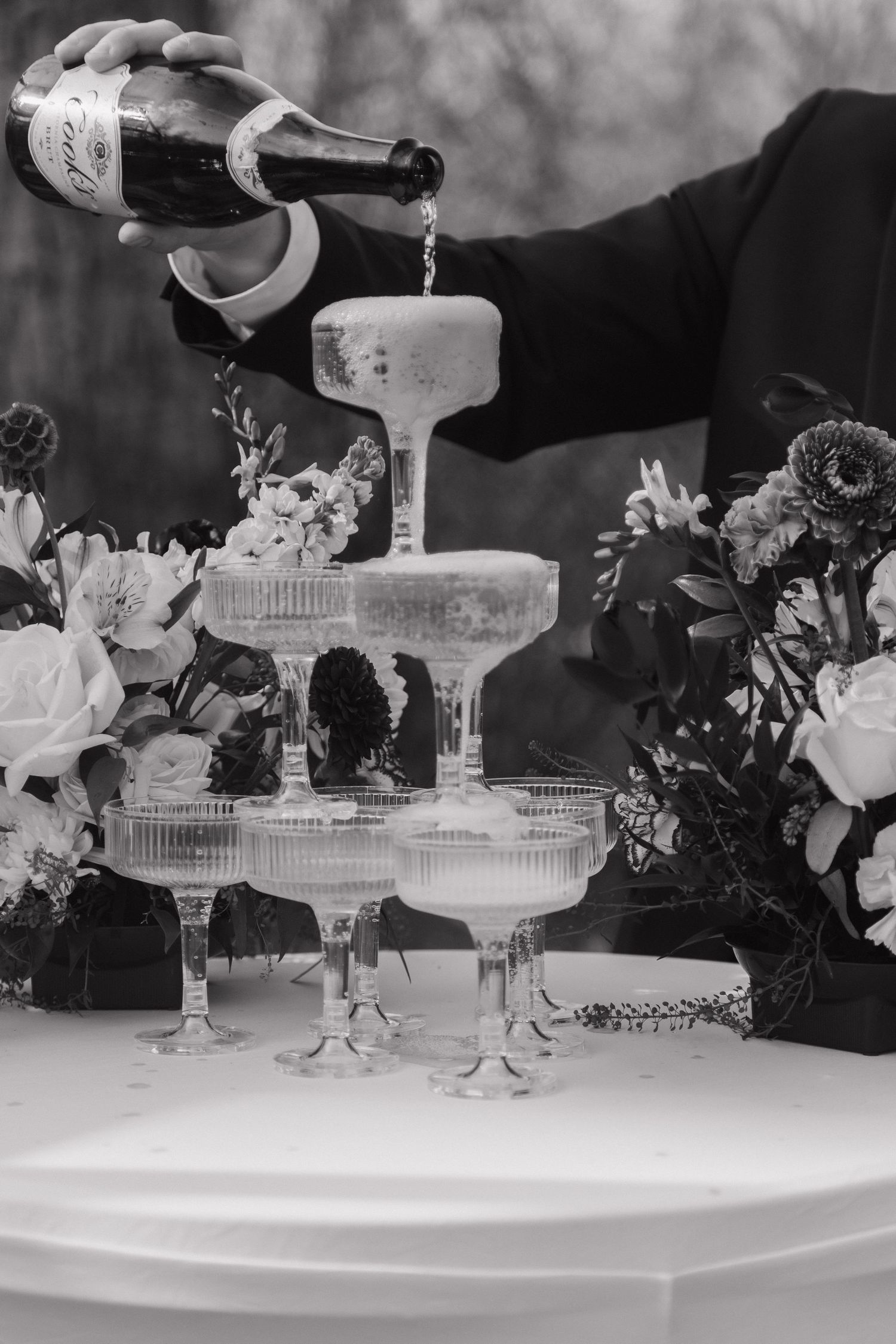 Black and white photo of champagne tower being filled at a wedding reception.