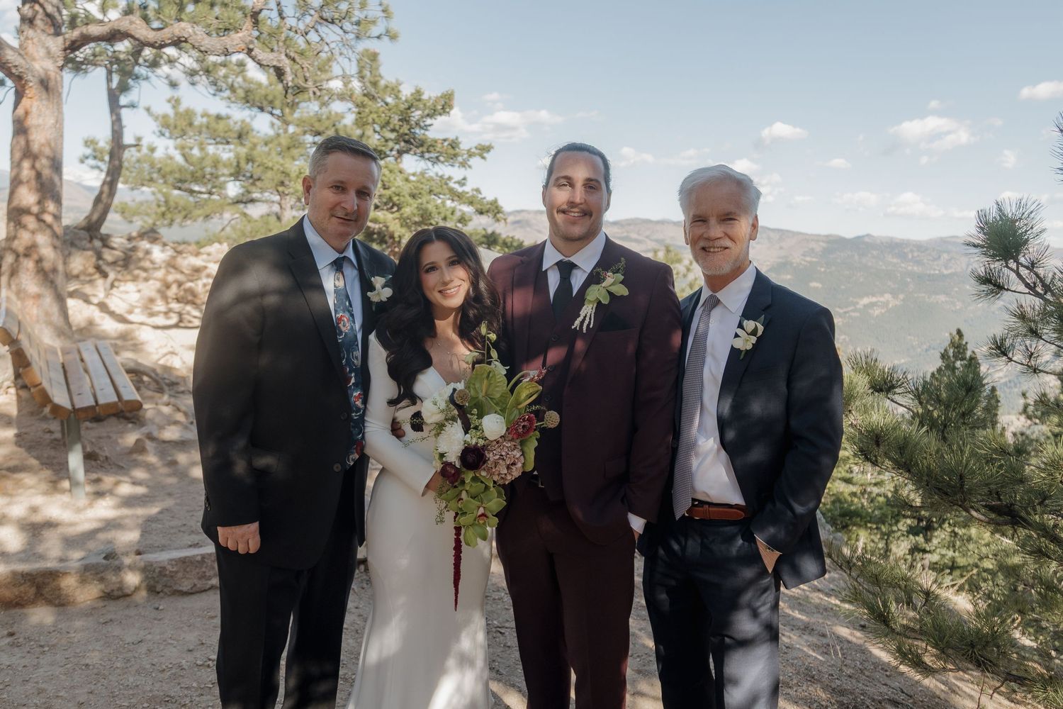 Wedding party portrait of bride and groom with two guests posing outdoors with mountain views behind them.