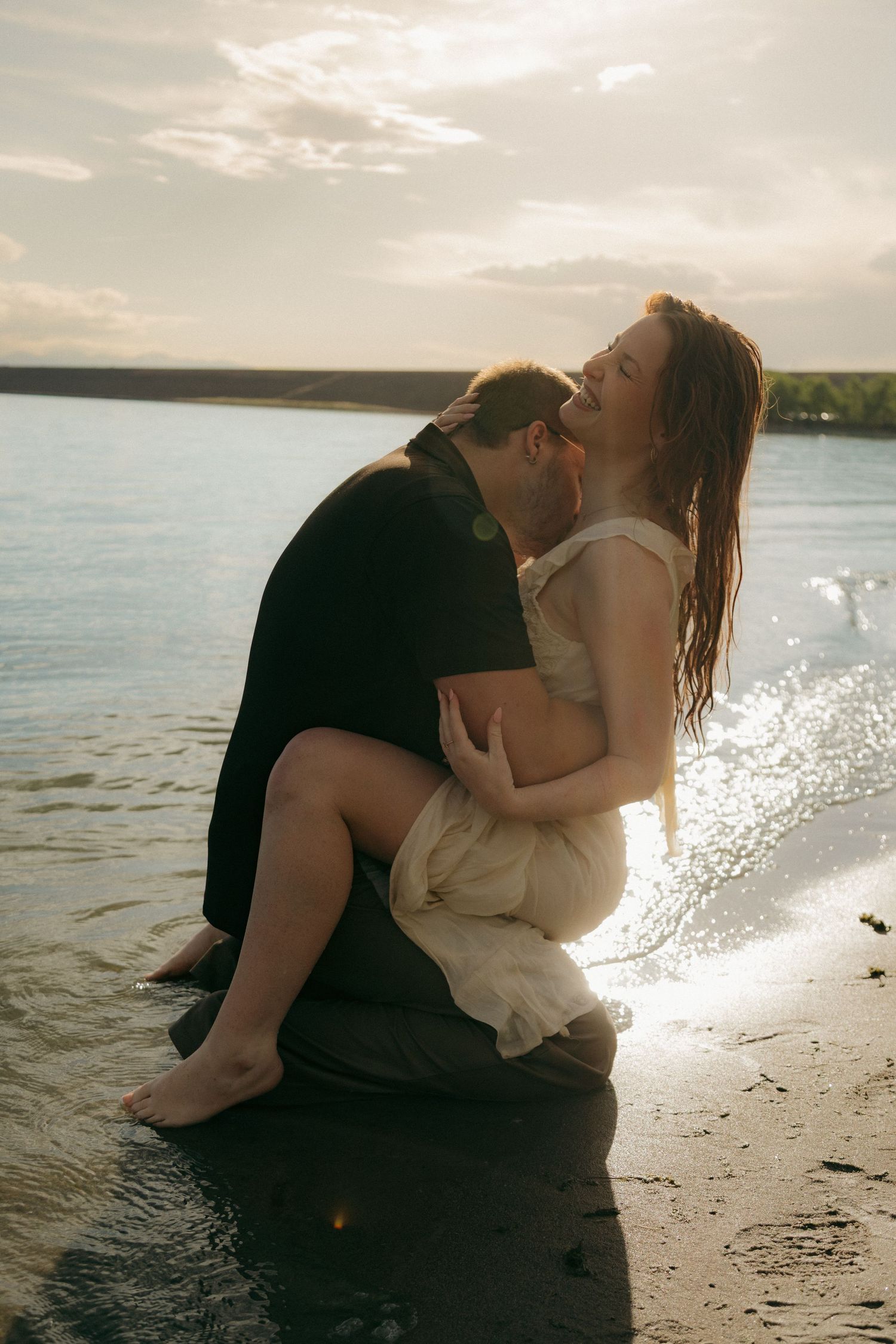 Man holding woman in his arms on a sandy beach shore at golden sunset.