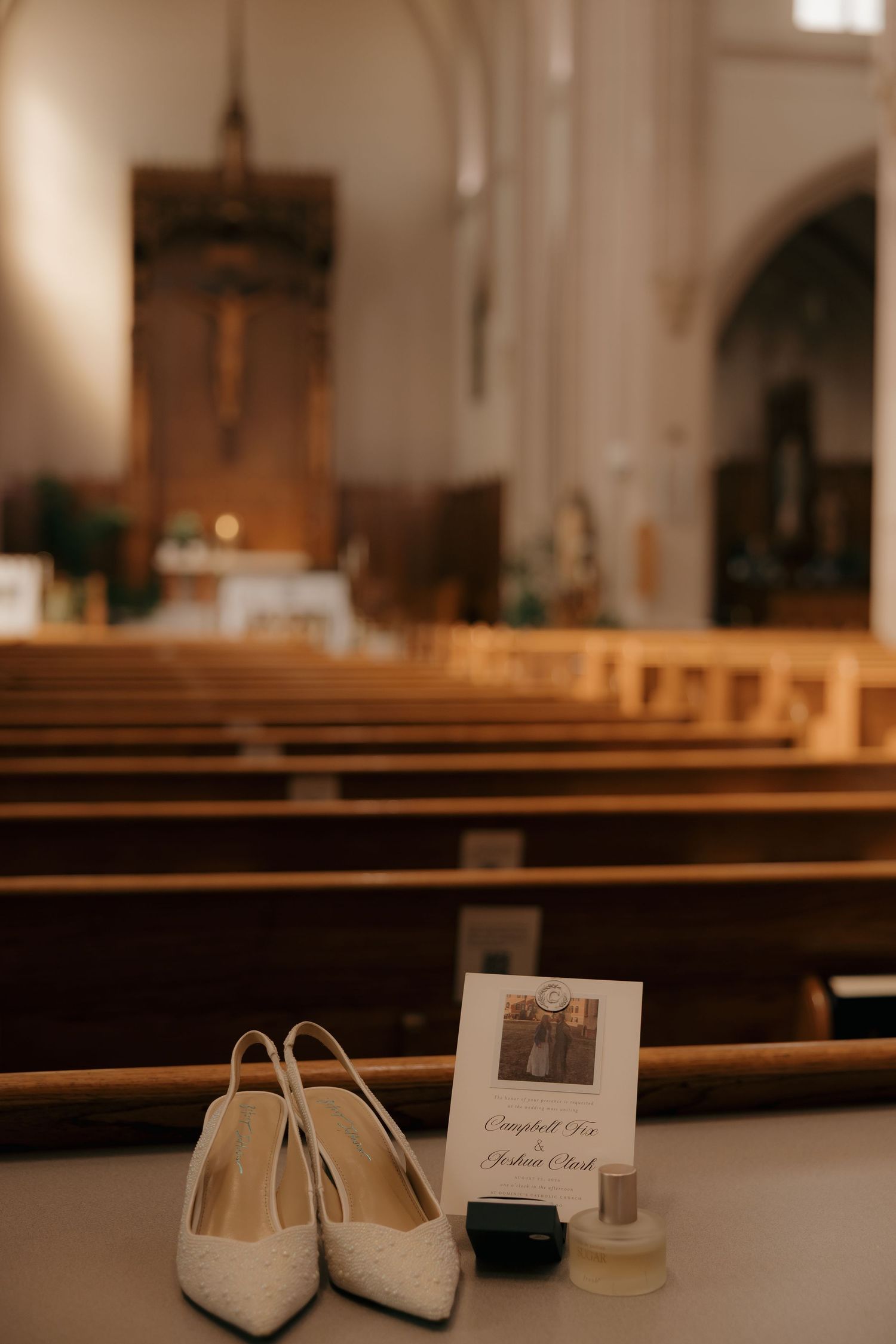 White bridal heels and perfume bottles rest on a church pew with a wedding program, elegant ceremony details in a classic church.