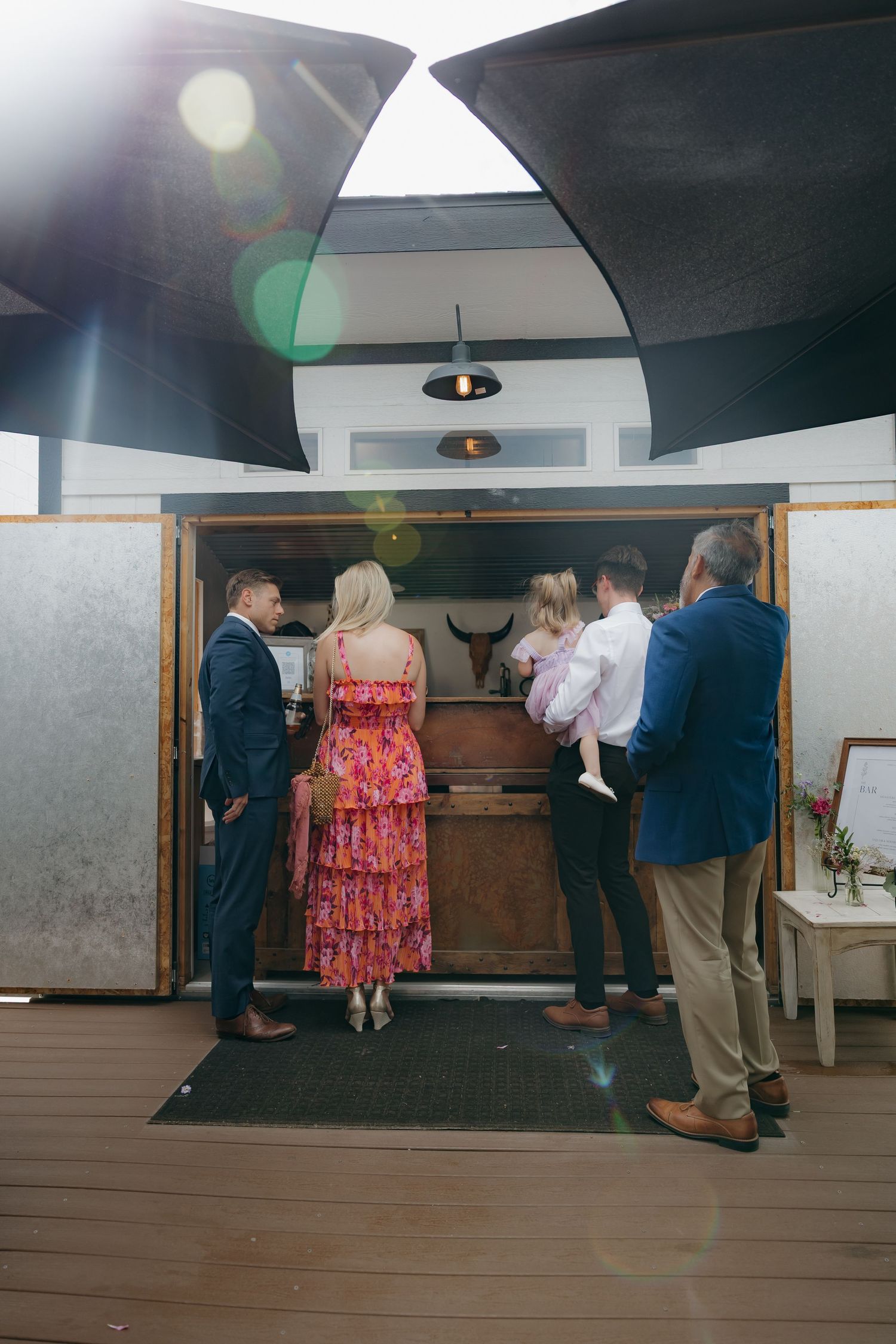 Wedding guests gather around a wooden bar inside a rustic venue with curved ceiling.