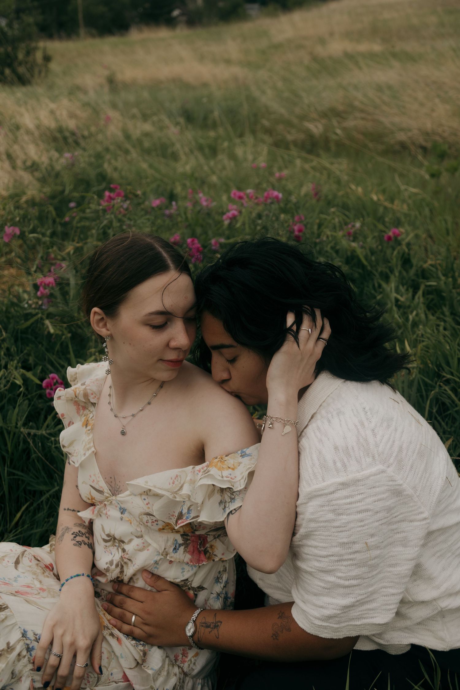 Romantic couple sitting in a wildflower meadow, sharing a tender embrace among pink blooms.
