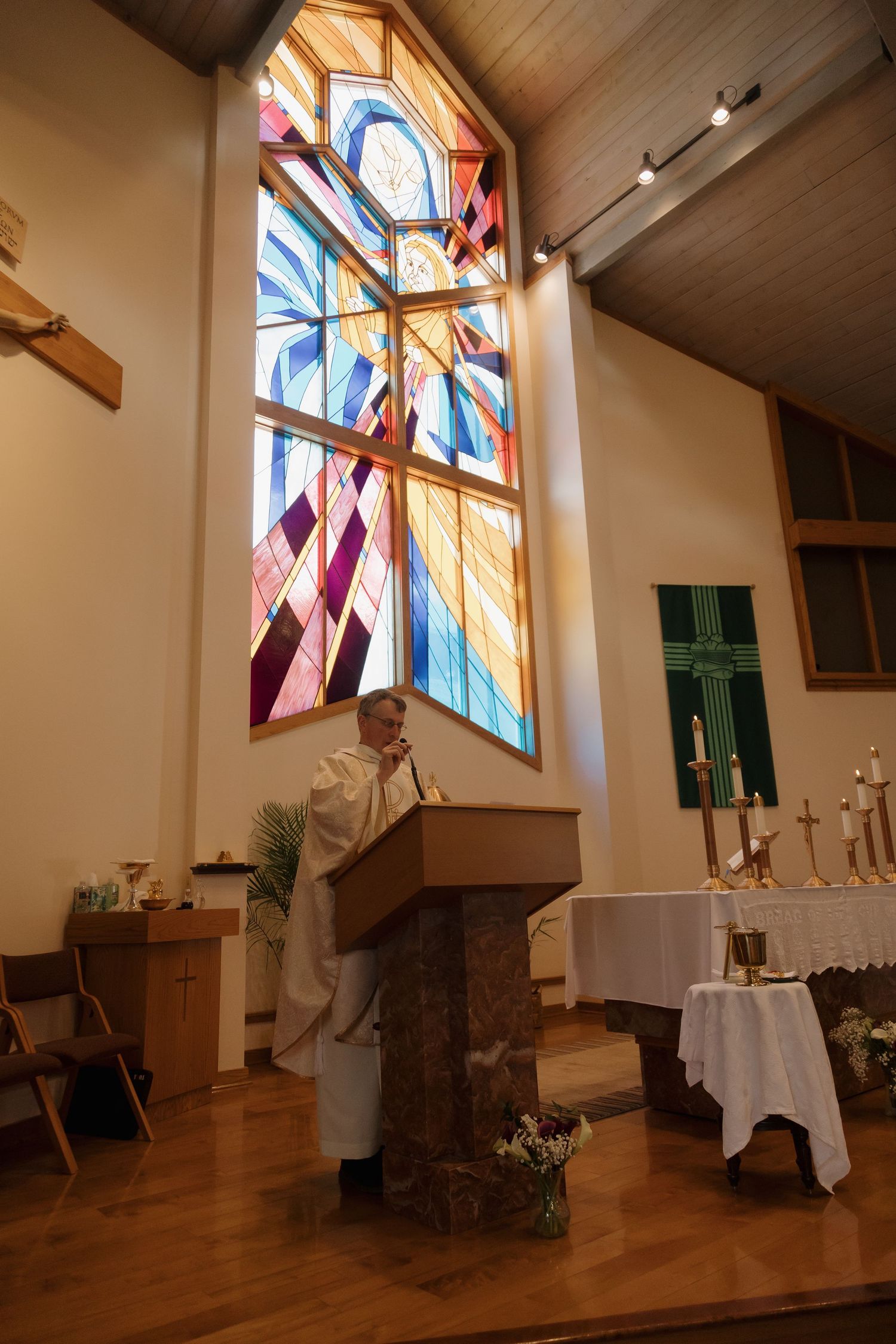 Priest delivering a sermon at a wooden pulpit in a Catholic church with colorful stained glass window.