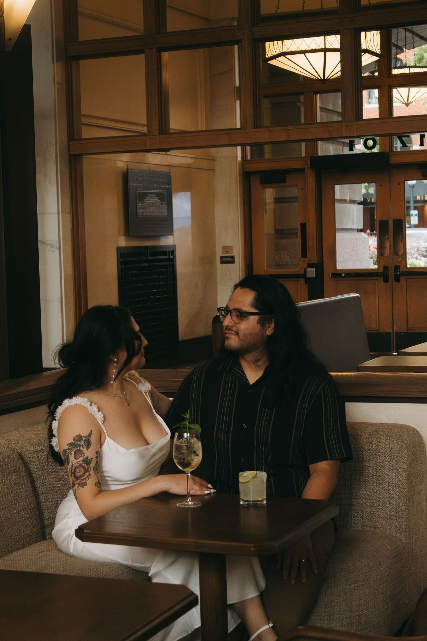 Two people sit at opposite ends of a booth in a dimly lit restaurant interior.