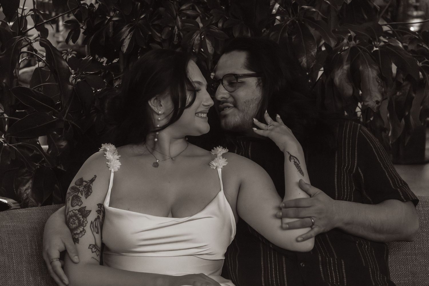 Black and white romantic portrait of couple sharing an intimate moment among foliage with vintage aesthetic.