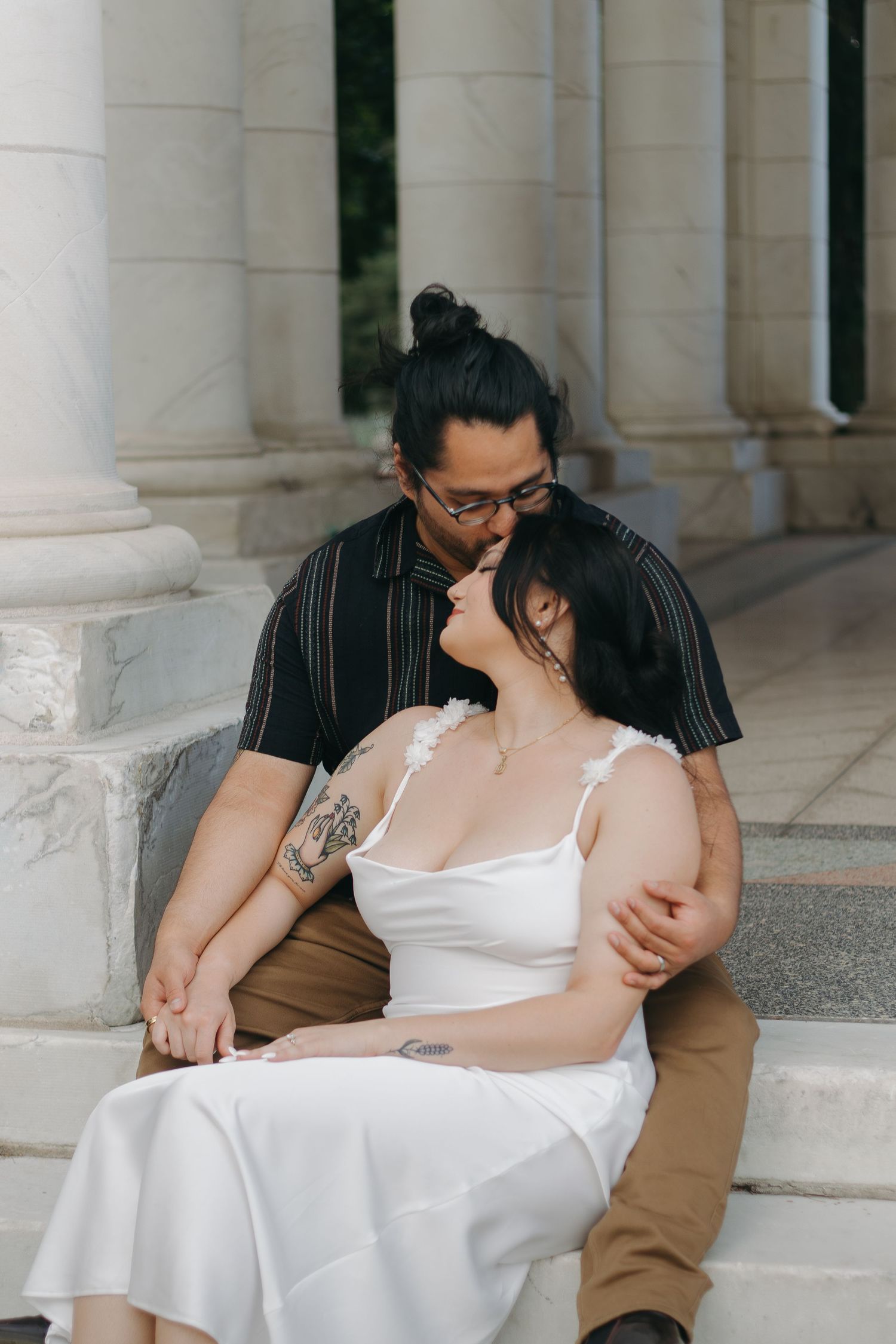 A romantic moment between a couple sitting on stone steps near classical columns.