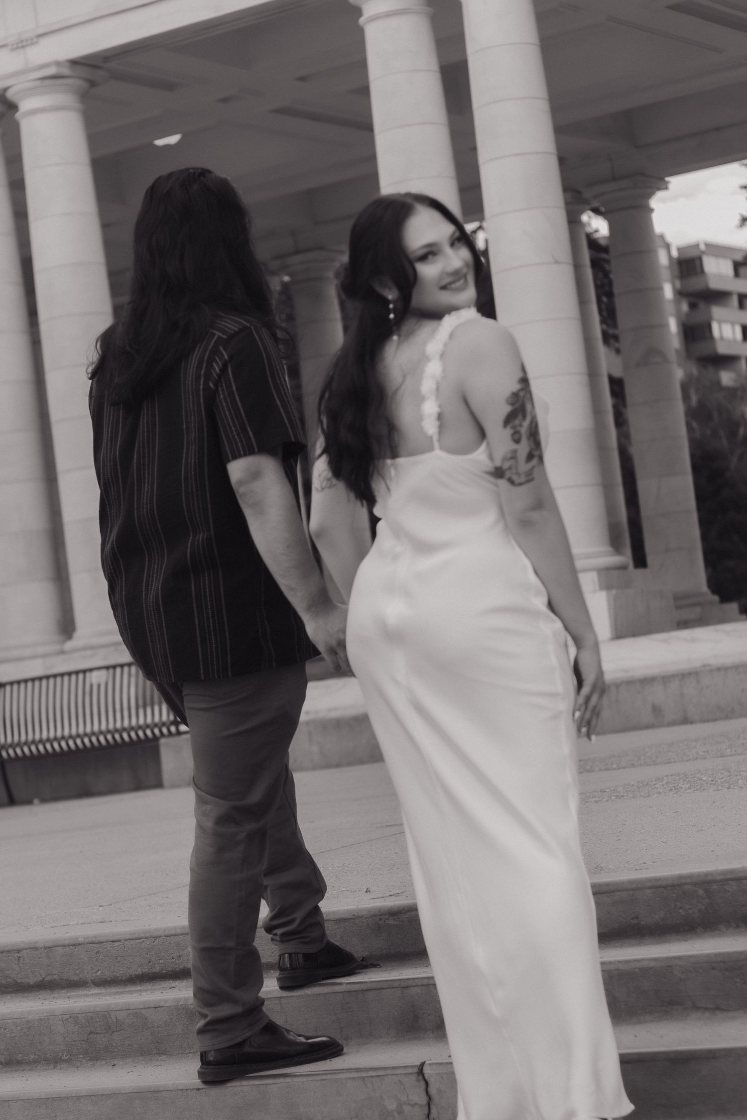 A black and white photo of a couple posing near white columns in formal attire.