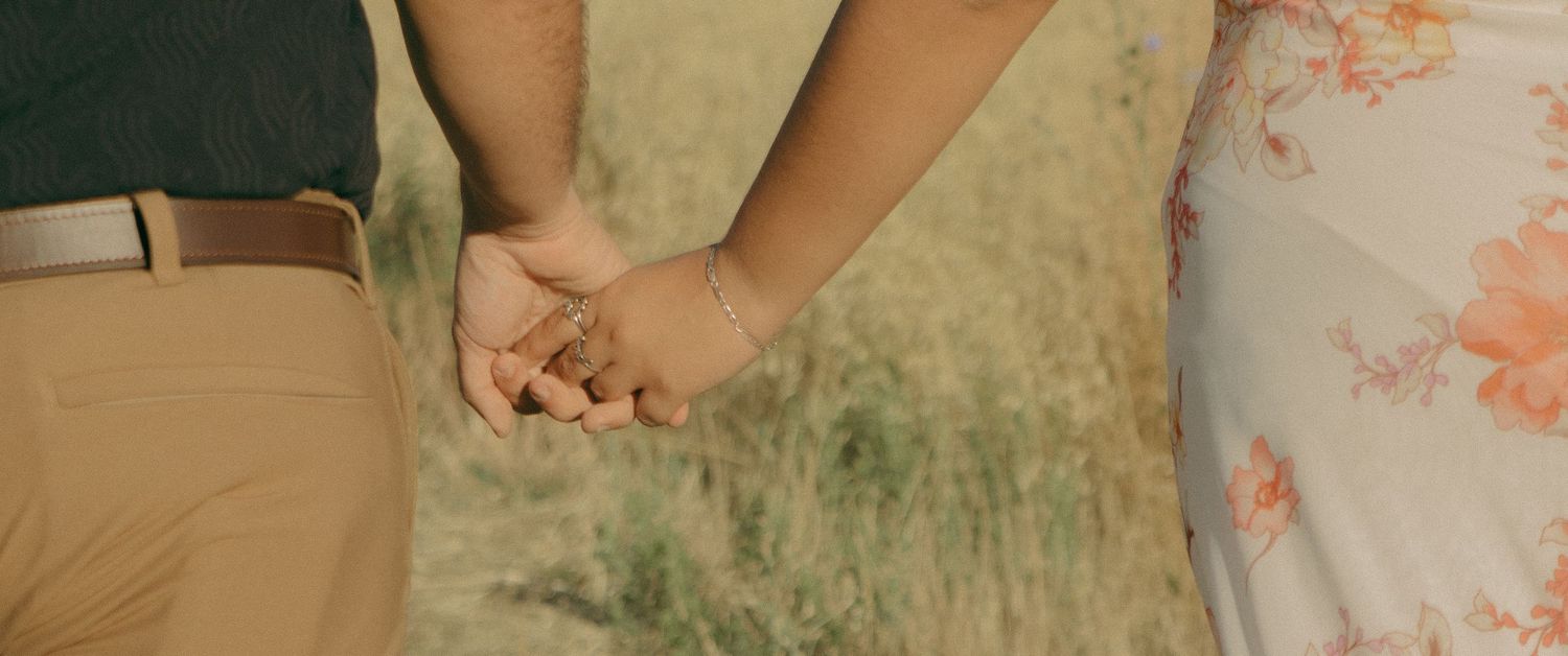 Close-up shot of two people holding hands in a field.