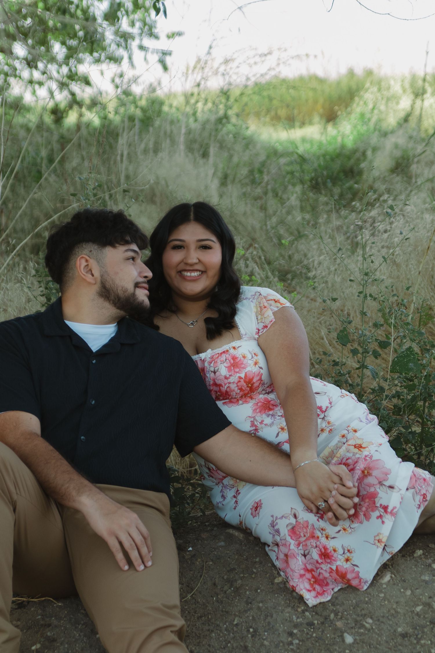 A couple shares a tender moment while sitting in nature surrounded by greenery.