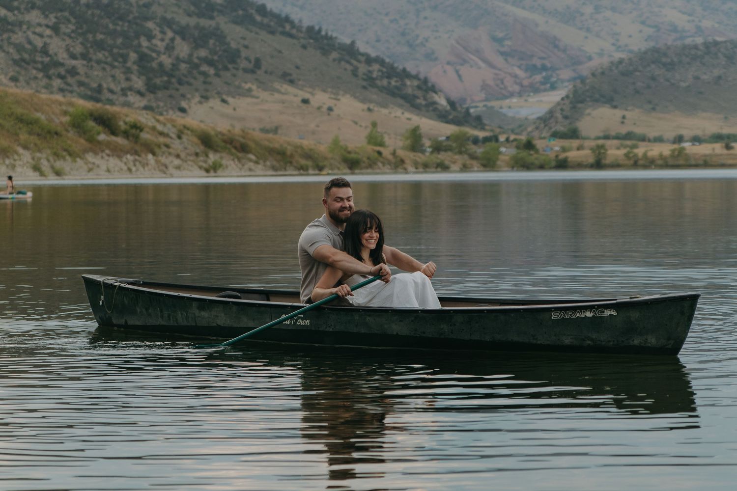 Wide landscape shot of mountain lake with couple paddling in distant canoe.
