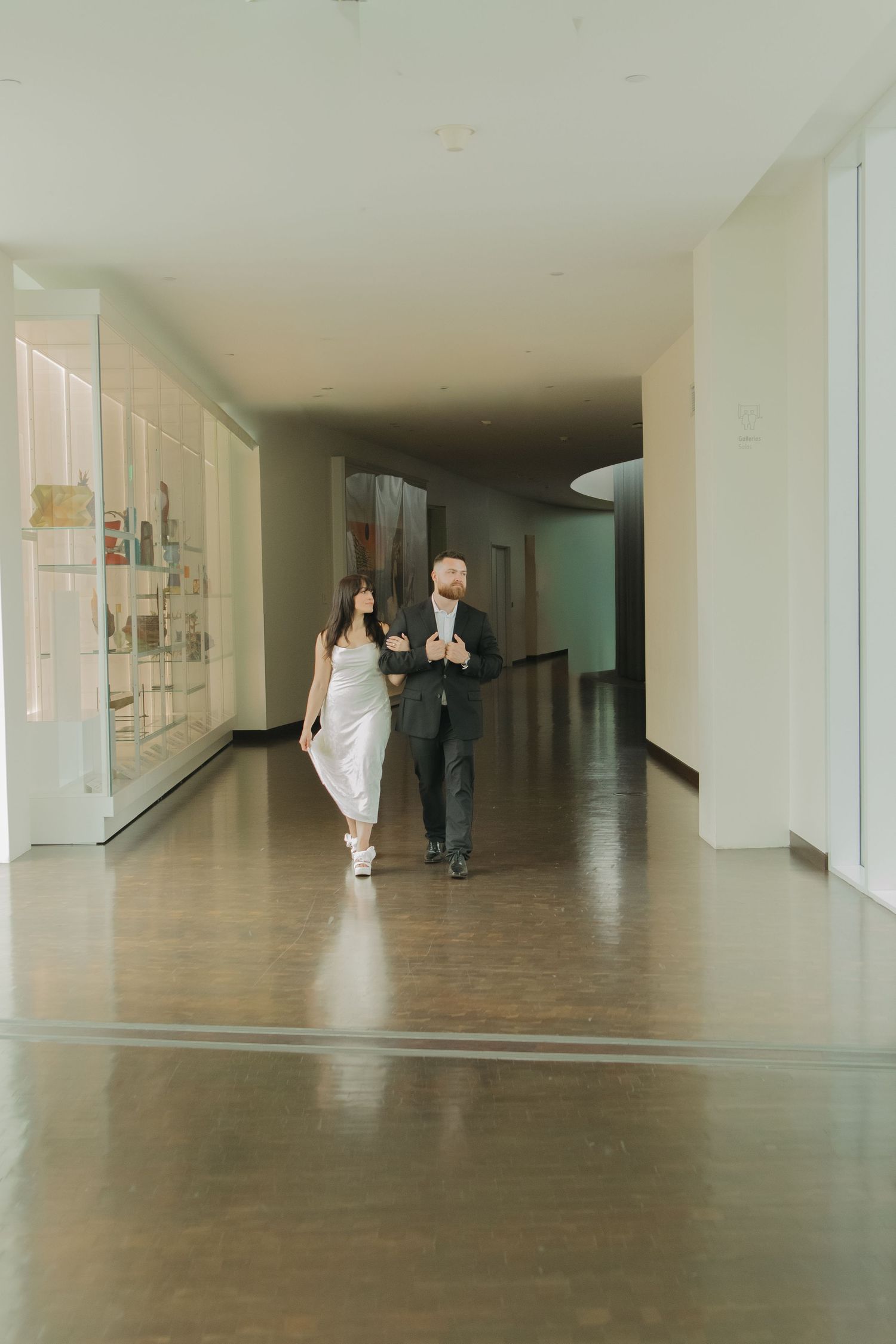 Modern gallery hallway with white walls and concrete floors showing distant figures.