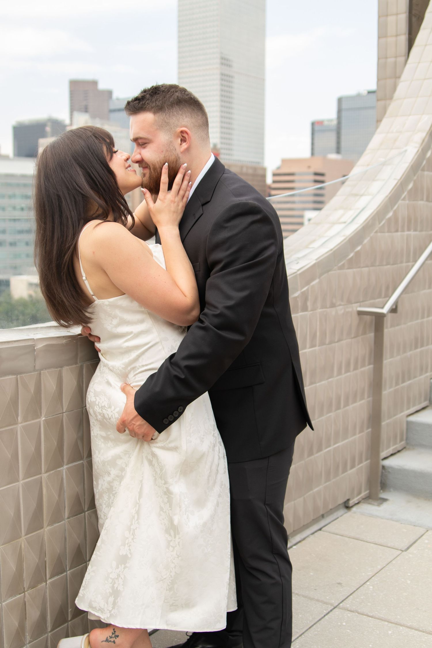 A romantic couple embraces on a rooftop terrace with city skyline in the background.