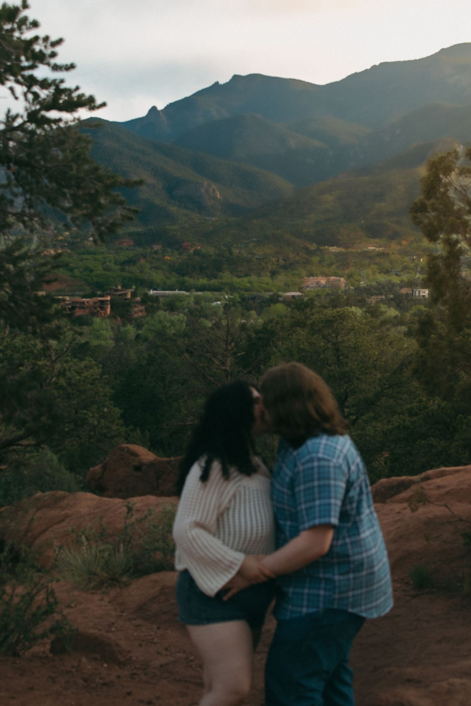 Two people embrace while overlooking a scenic mountain valley during golden hour.