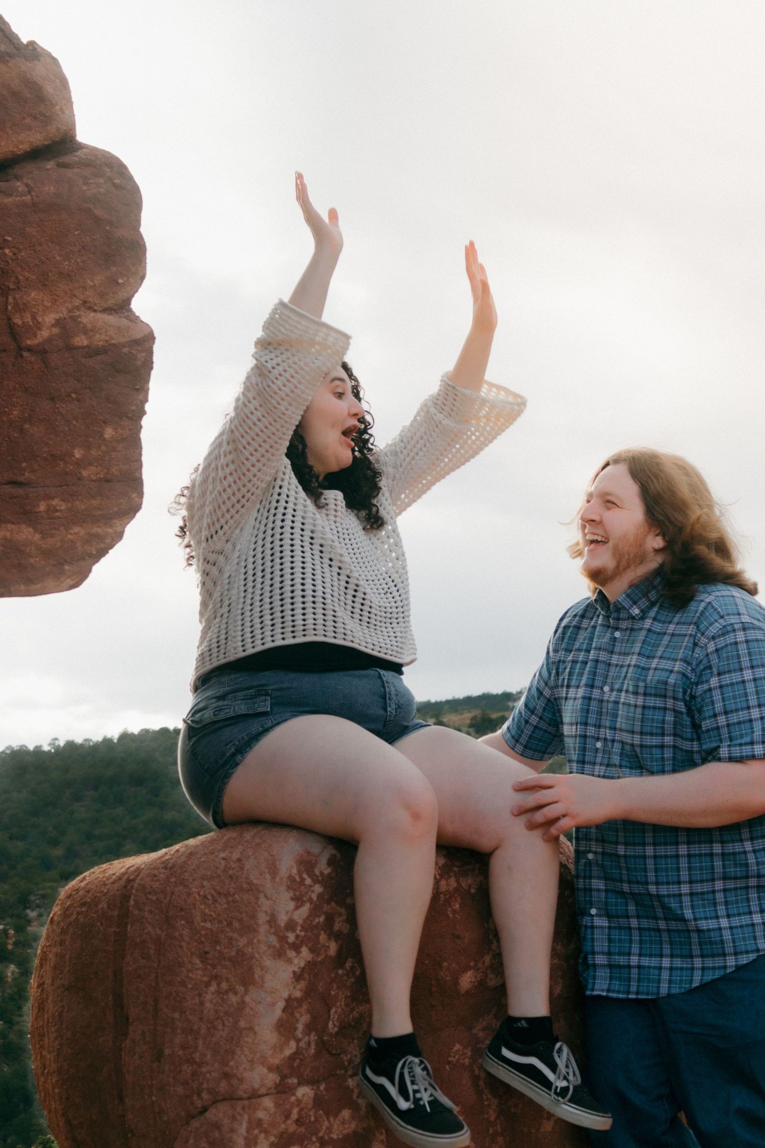 A joyful moment captured as a couple plays and laughs on red rocks in nature.