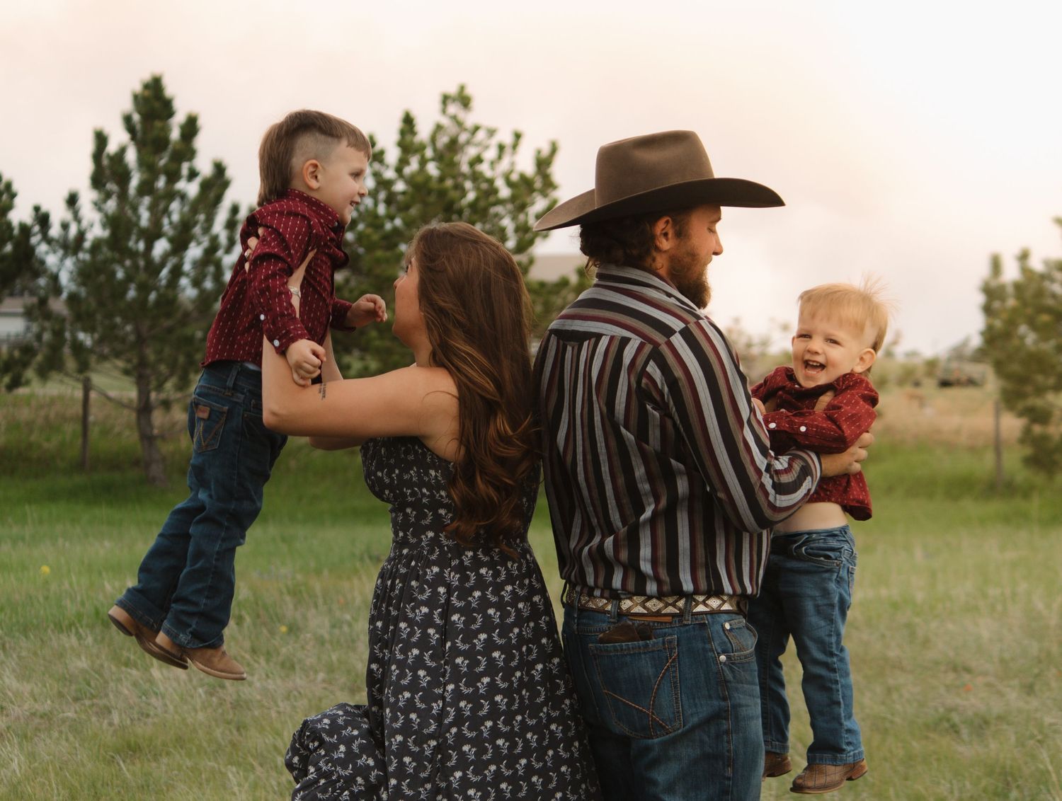 Candid family moment captured in golden hour light as parents hold their children in a field.
