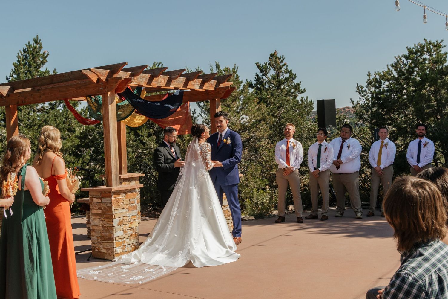 Wedding ceremony setup with wooden pergola and mountain views on a sunny day.