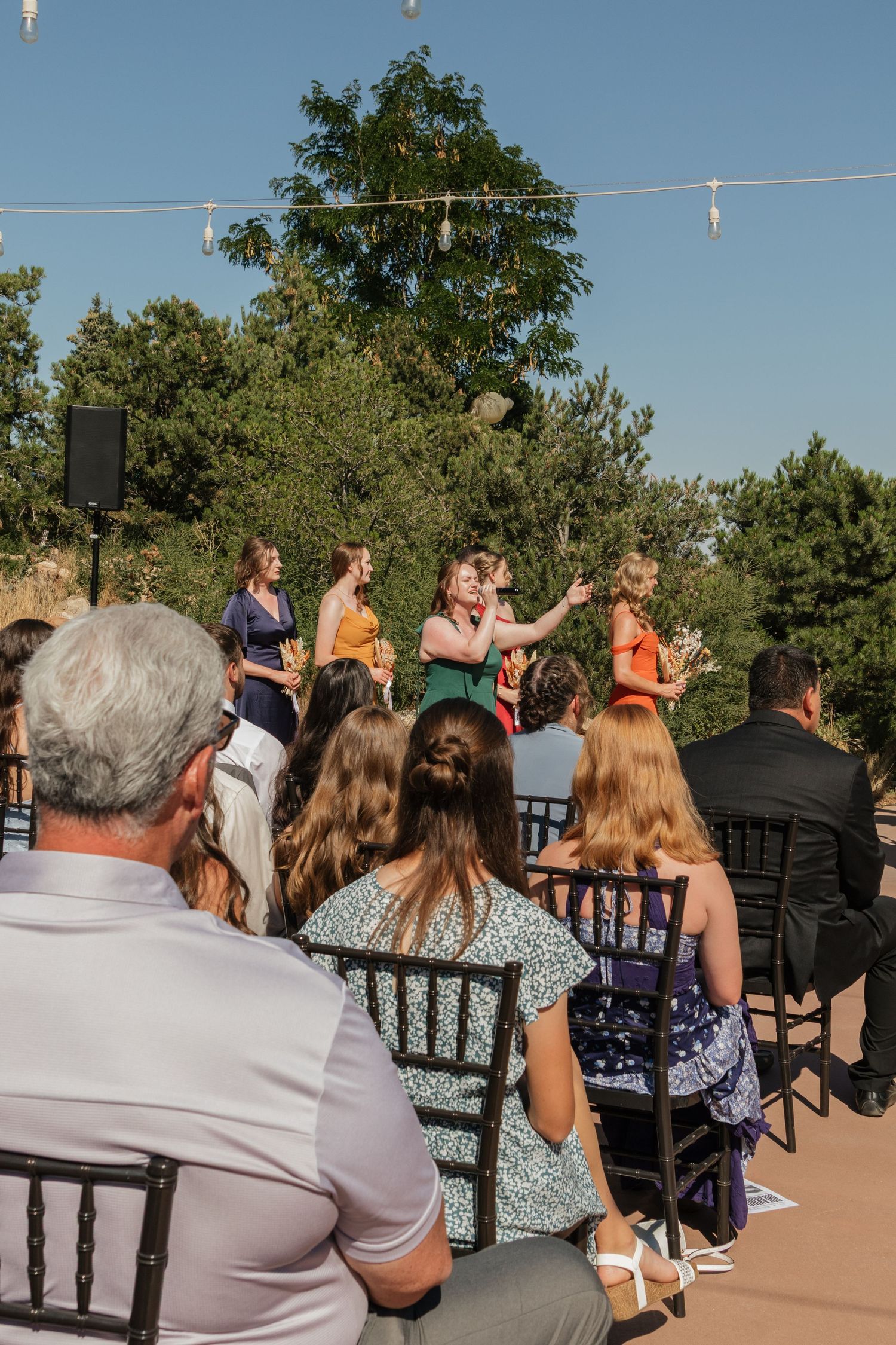 Wedding guests seated outdoors on dark wooden chairs against a scenic mountain backdrop.