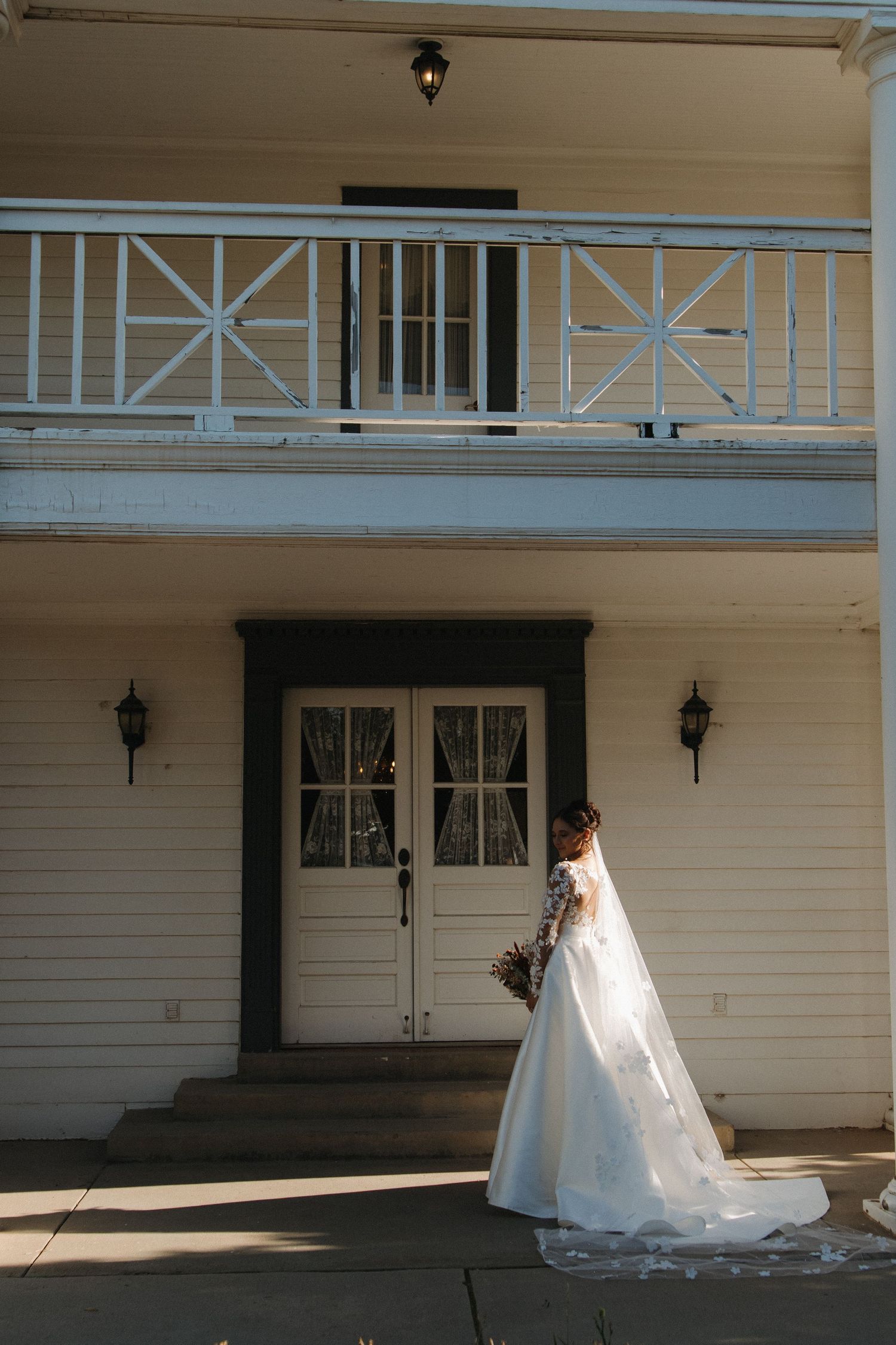 White wedding gown silhouette against classic white building with dark trim.