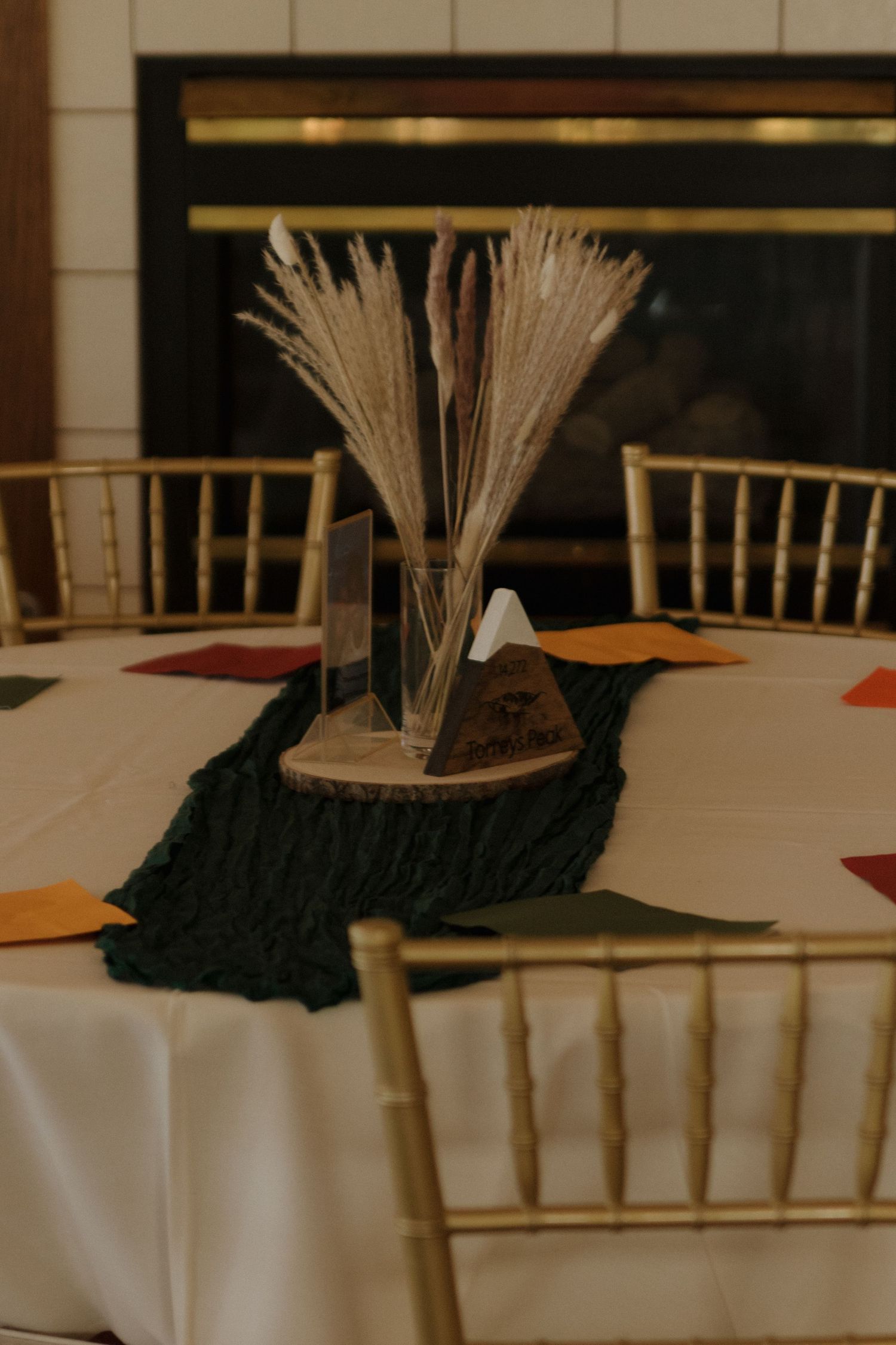 Rustic wedding centerpiece with wheat stalks on a dark runner and white tablecloth.