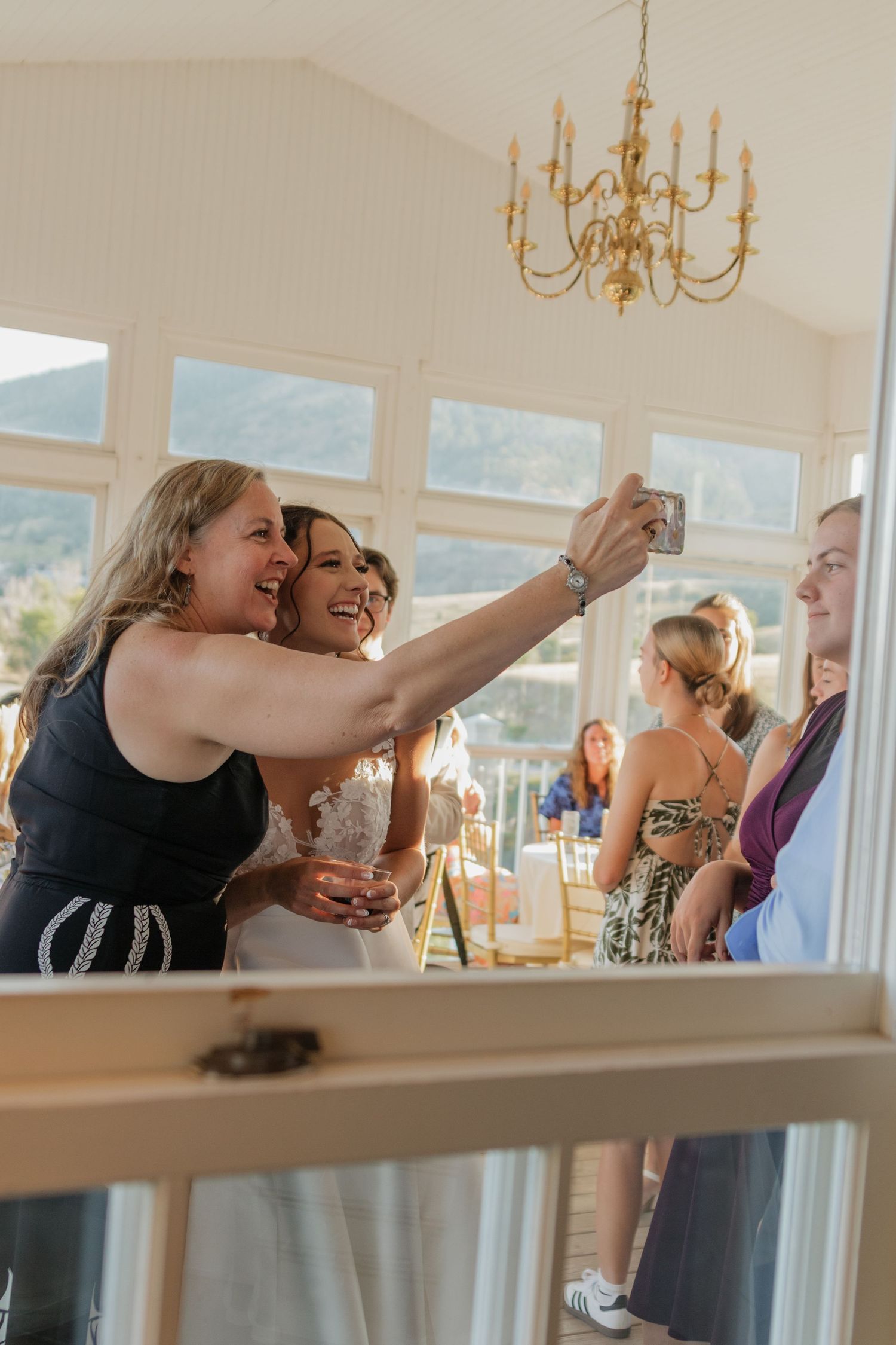 Wedding guests laughing and taking selfies during reception celebration.