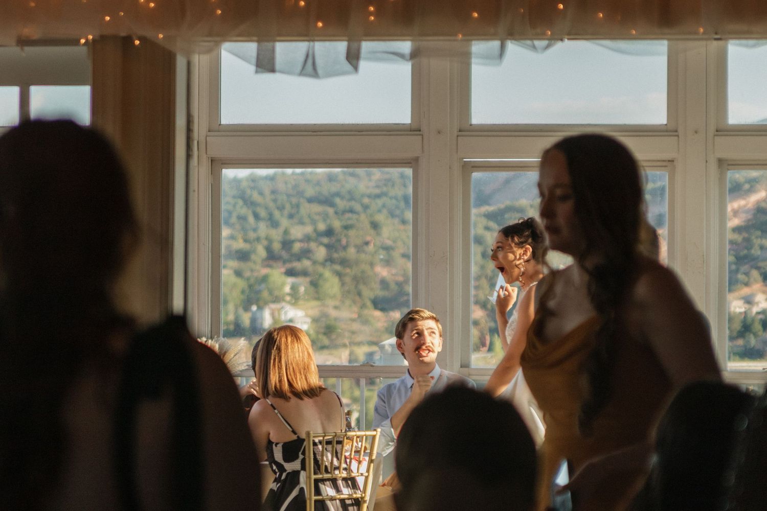 Soft silhouettes of wedding guests against large windows during sunset.