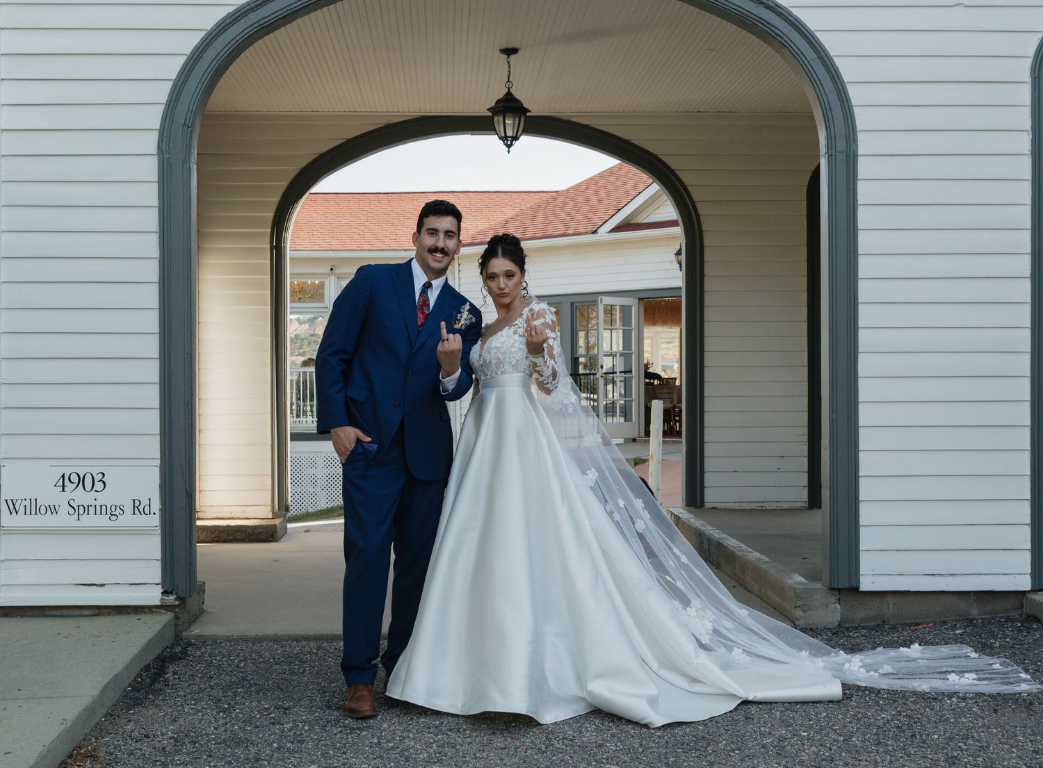 Wedding couple poses under white arched doorway of a traditional building.
